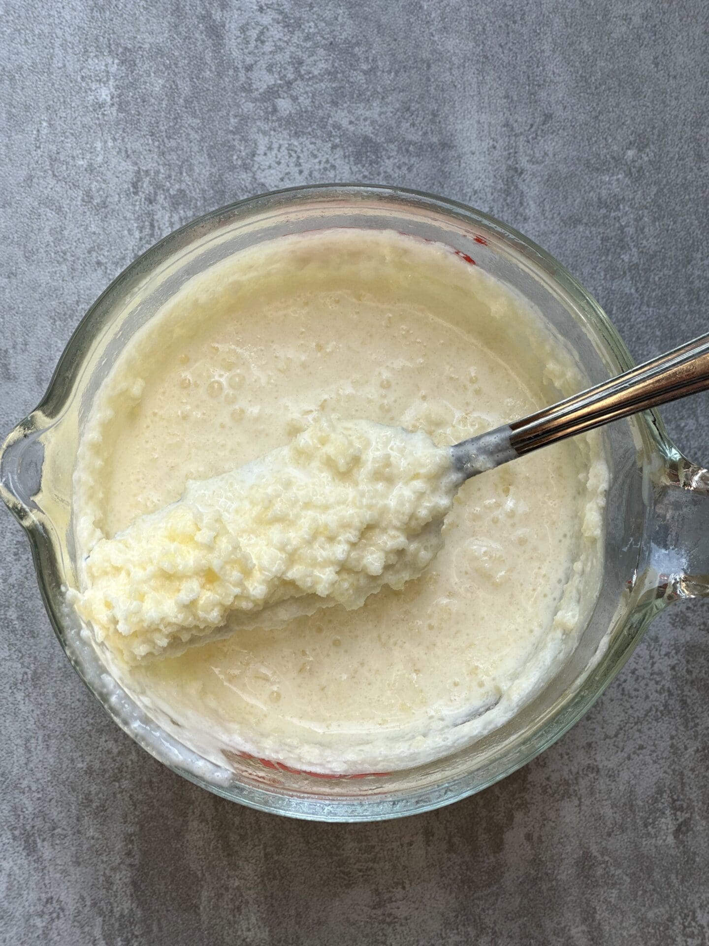 A glass pitcher seen from above, containing cold cream mixed with melted butter to form a lumpy mixture to be added to scone batter.