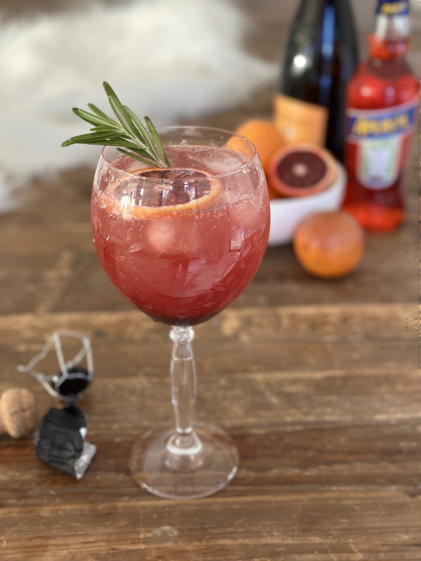 IMG_9865 A blood orange and black currant Aperol spritz garnished with rosemary sits on a wood table