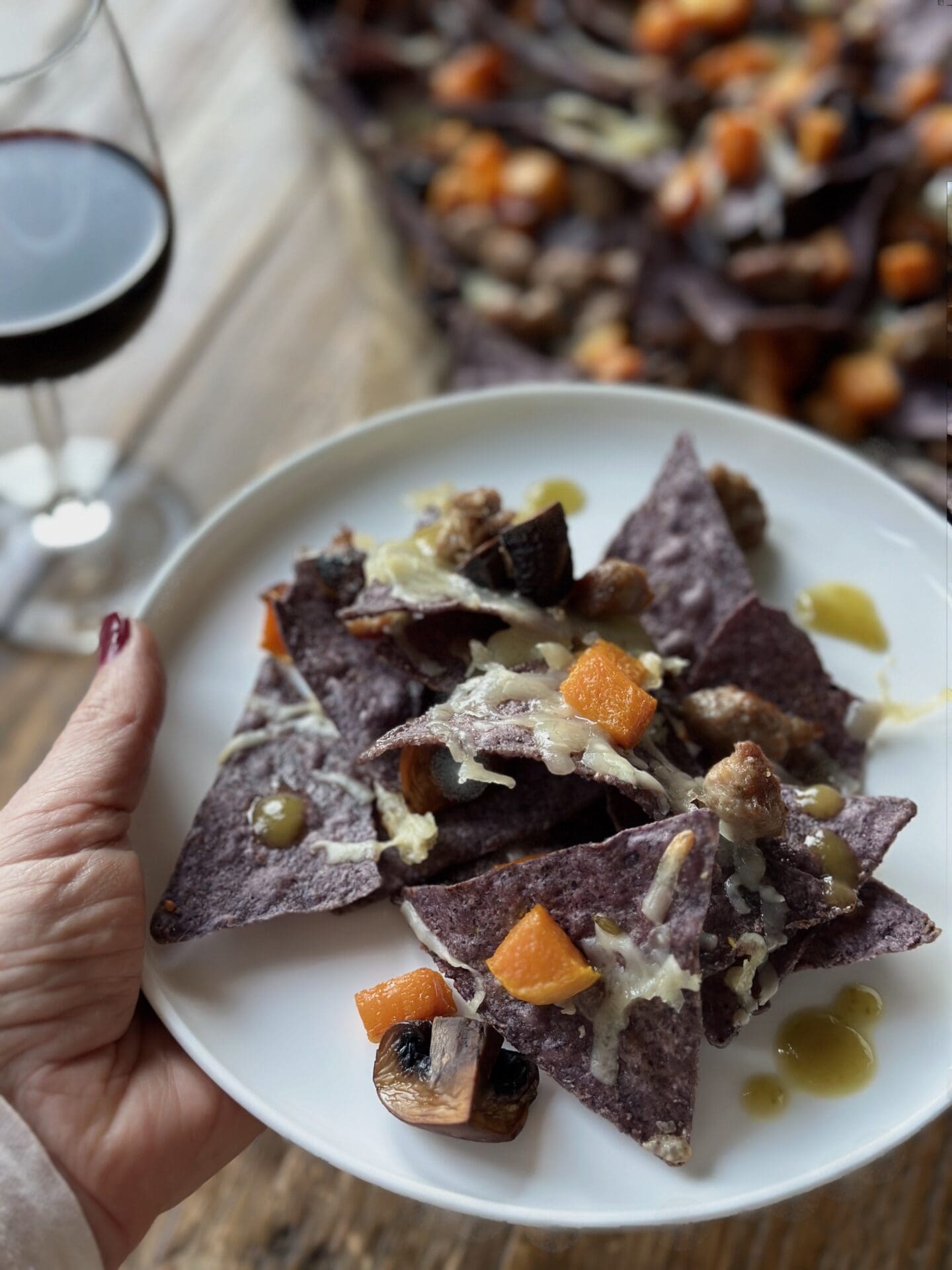 IMG_0278 A hand holds a plate of blue corn harvest nachos in front of a glass of red wine