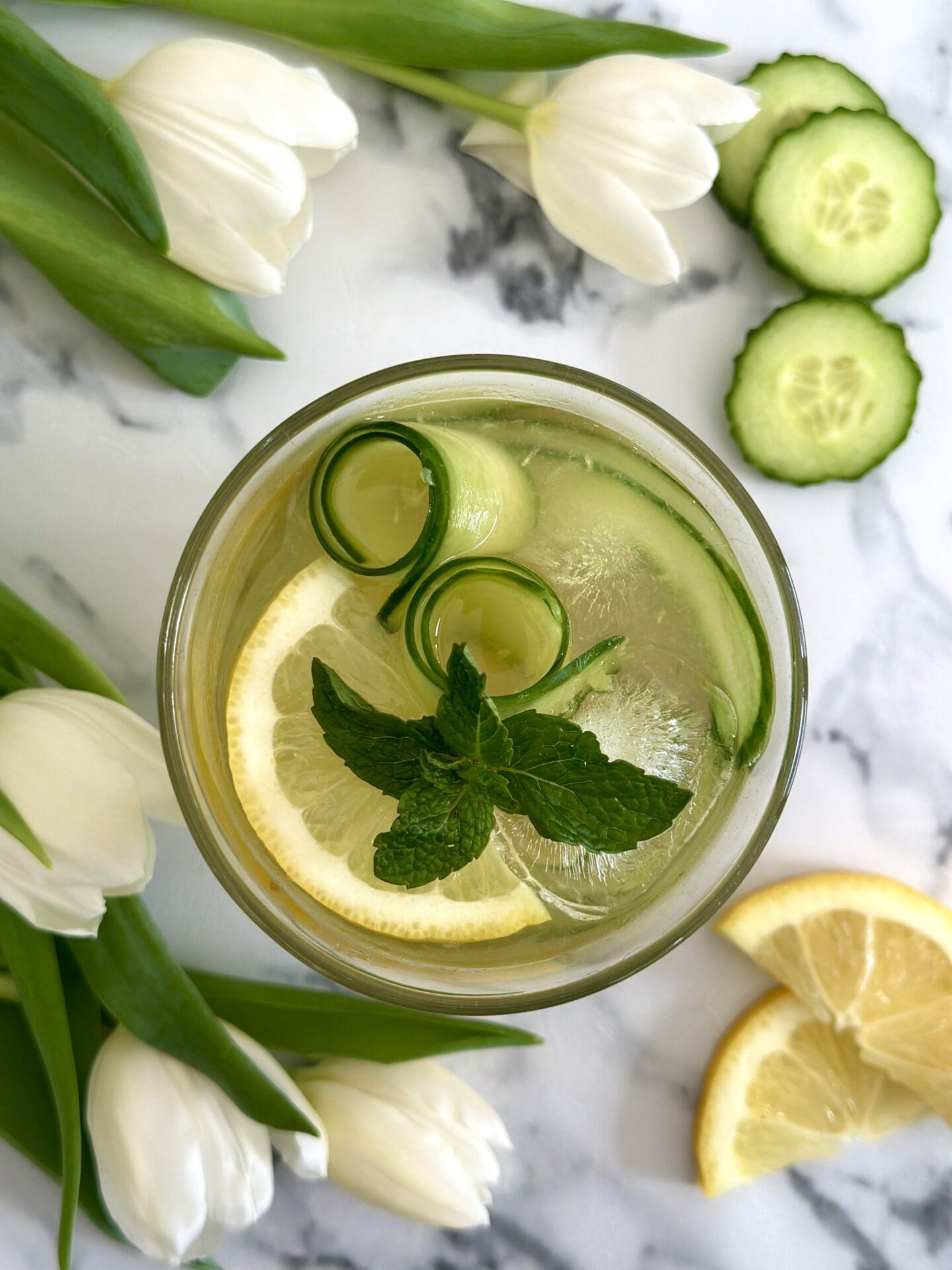 IMG_1355 An Irish Maid cocktail is seen from above surrounded by cucumber slices, lemon slices and white tulips