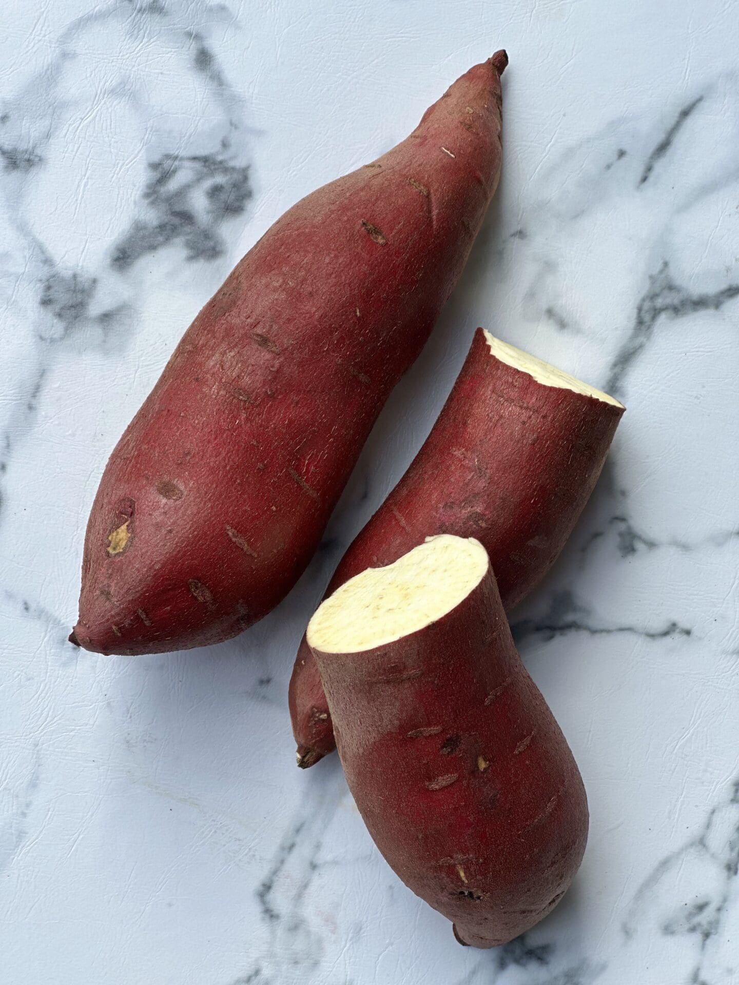 IMG_6960 Two Japanese sweet potatoes are seen from above, one is whole and one is cut in half exposing the creamy interior