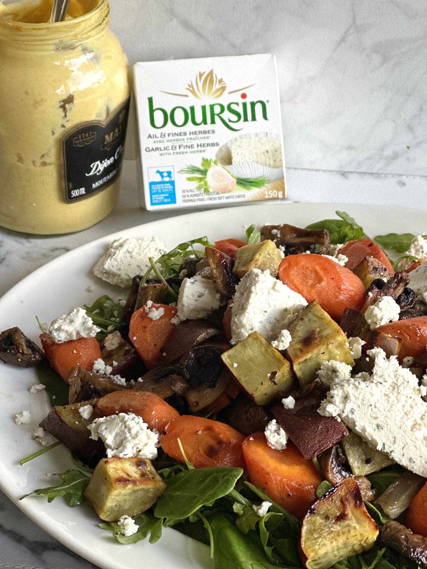 IMG_6971 A platter of Warm Roasted Vegetable and Boursin Salad is seen from the side with a package of Boursin cheese and a jar of dijon mustard seen in the background.