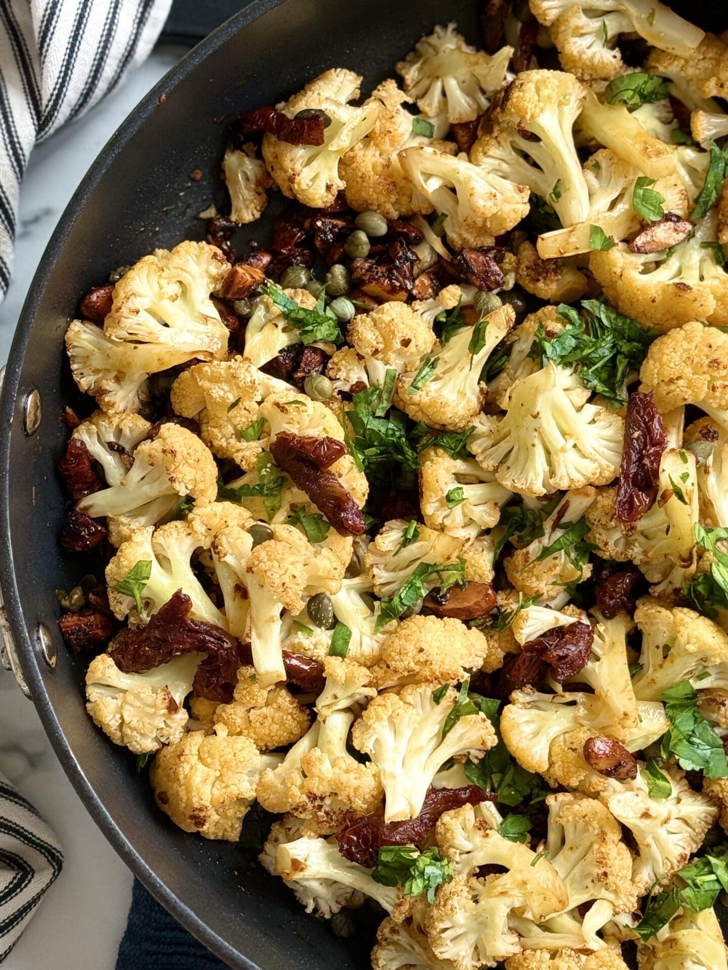 A black pan of Roasted Cauliflower with Sundried Tomatoes, Capers and Crunchy Almonds is seen from above.