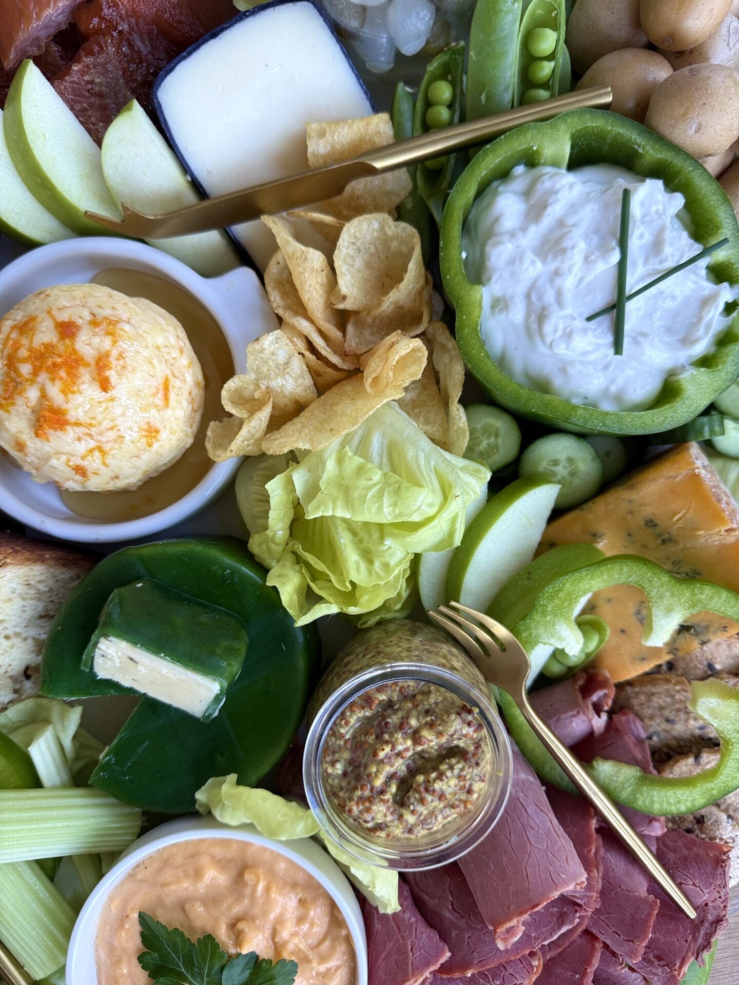A St Patrick's Day Charcuterie Board is seen close up, from above. The board features green vegetables, oranges cheeses and white dip, representing the colours of the Irish flag.
