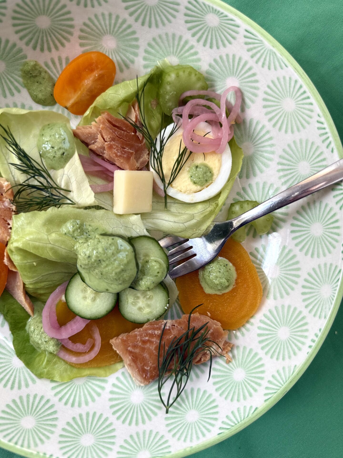 An individual serving of Irish Pub Salad with Hot Smoked Salmon is seen from above in a green and white patterned bowl. The salad features tender green lettuce, crisp veggies, pickled golden beets, sliced eggs, hot smoked salmon and pickled red onions.