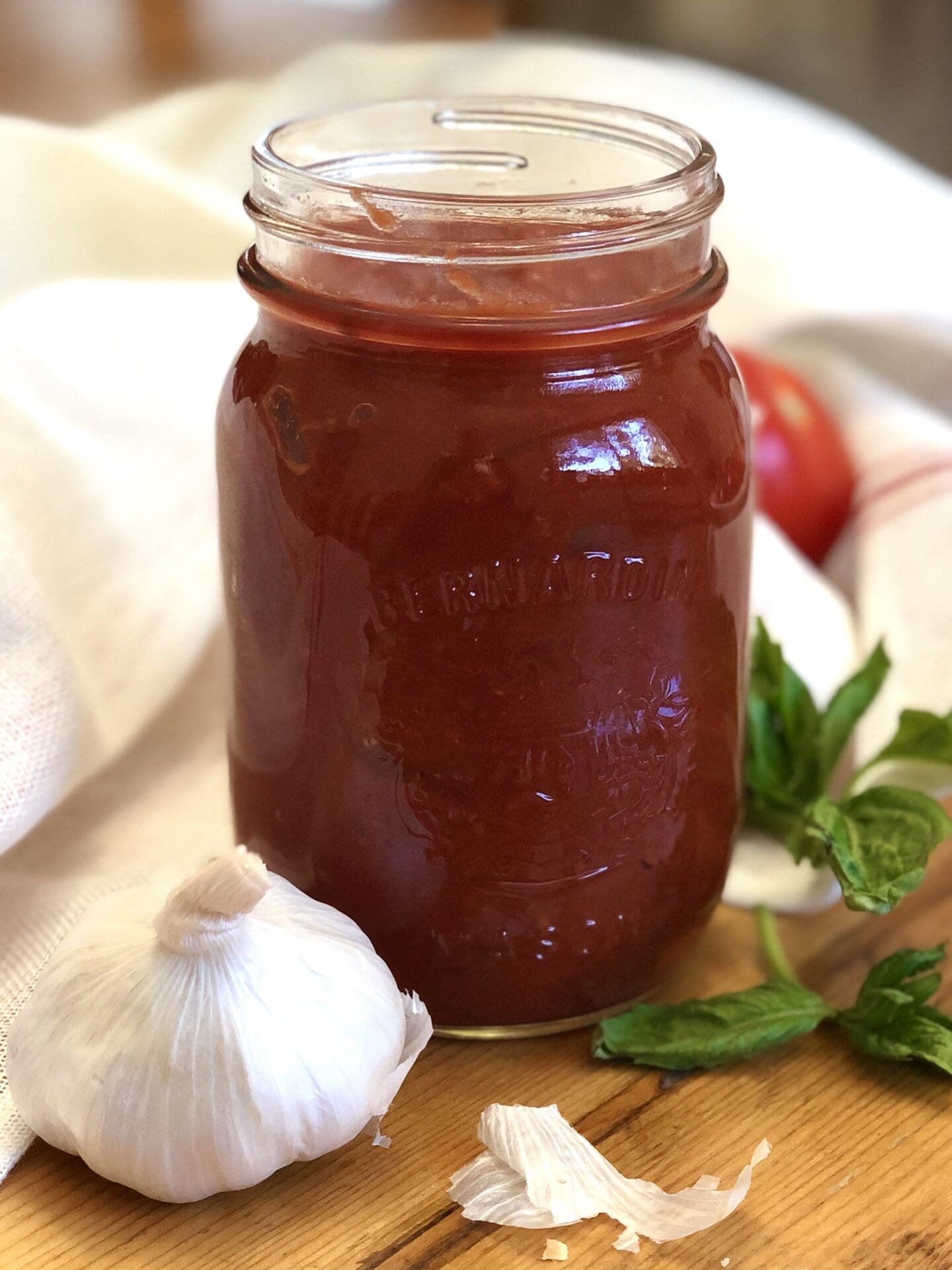 IMG_3144 A jar of homemade Sarah's Marinara Sauce is seen on a aged wood table alongside fresh garlic, tomatoes and basil.