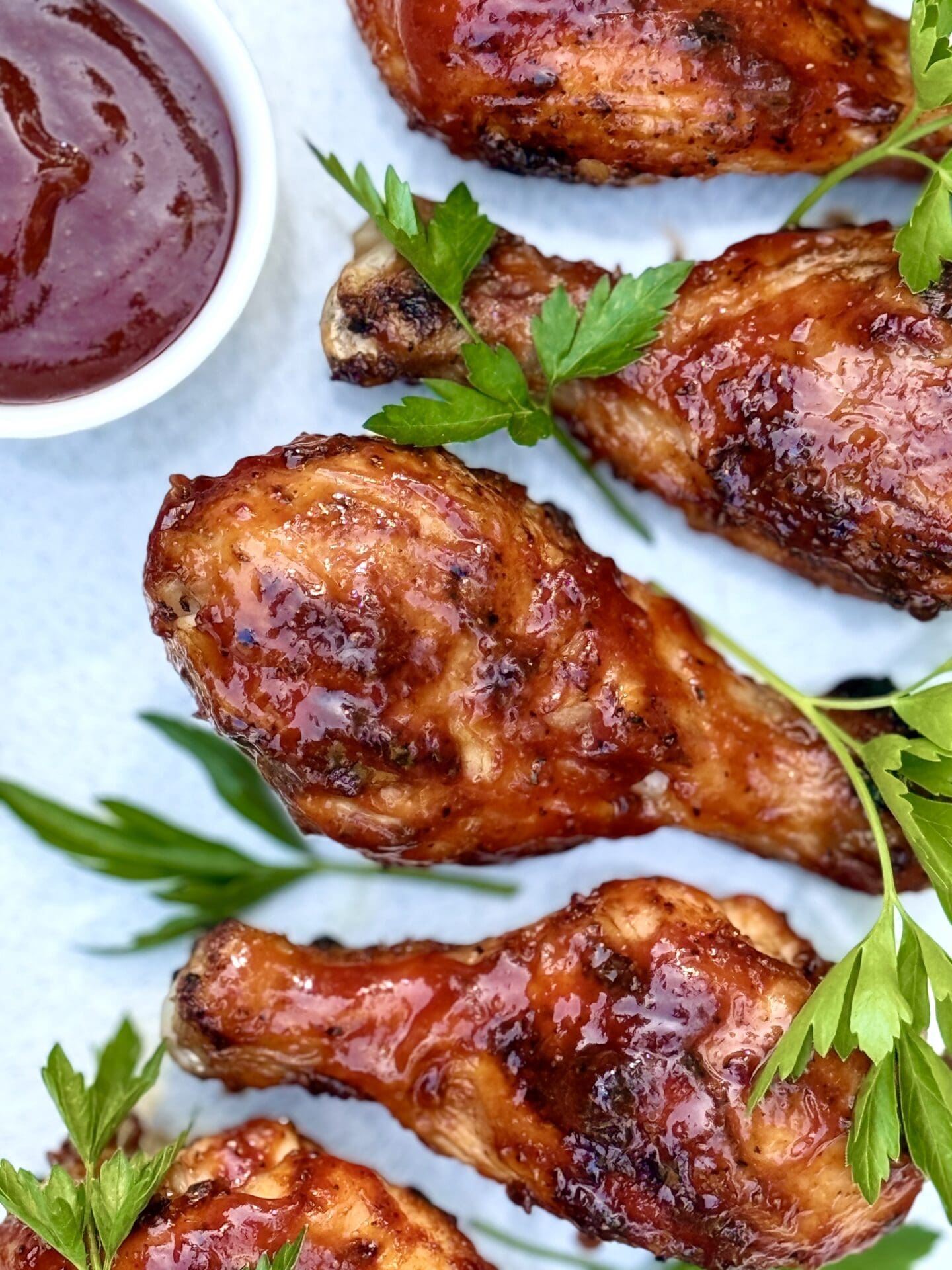 IMG_5938 Smokey Sweet Grilled Chicken Legs are seen from above, on a platter, garnished with a small dish of barbecue sauce and a sprinkling of fresh parsley.