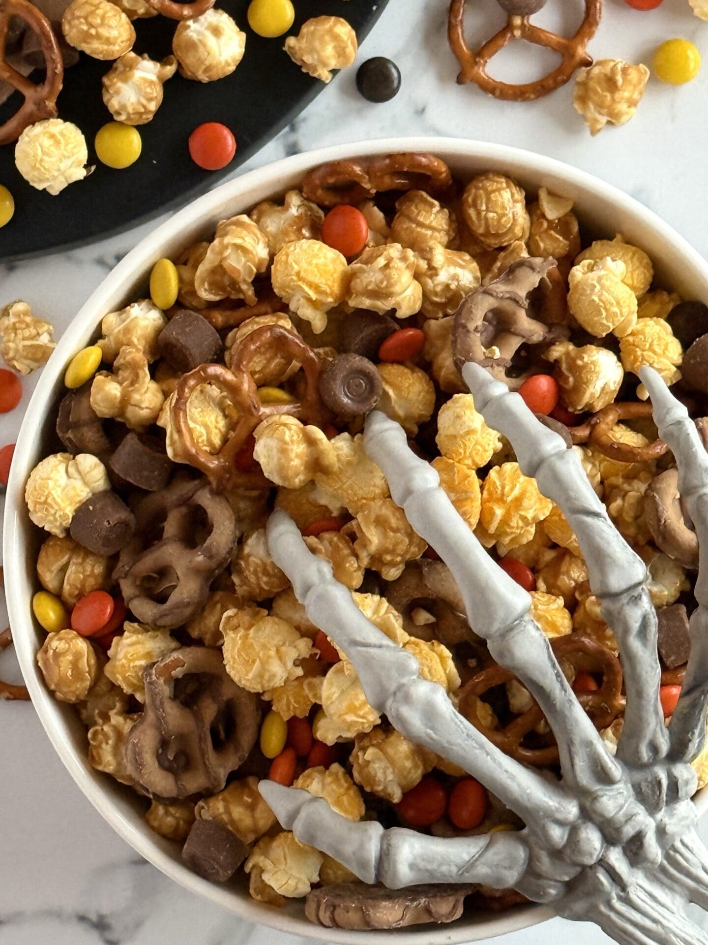 IMG_7125 Sweet and salty Monster Munch Halloween Snack Mix is seen spilling over onto the counter. A bony hand reaches in from the corner.