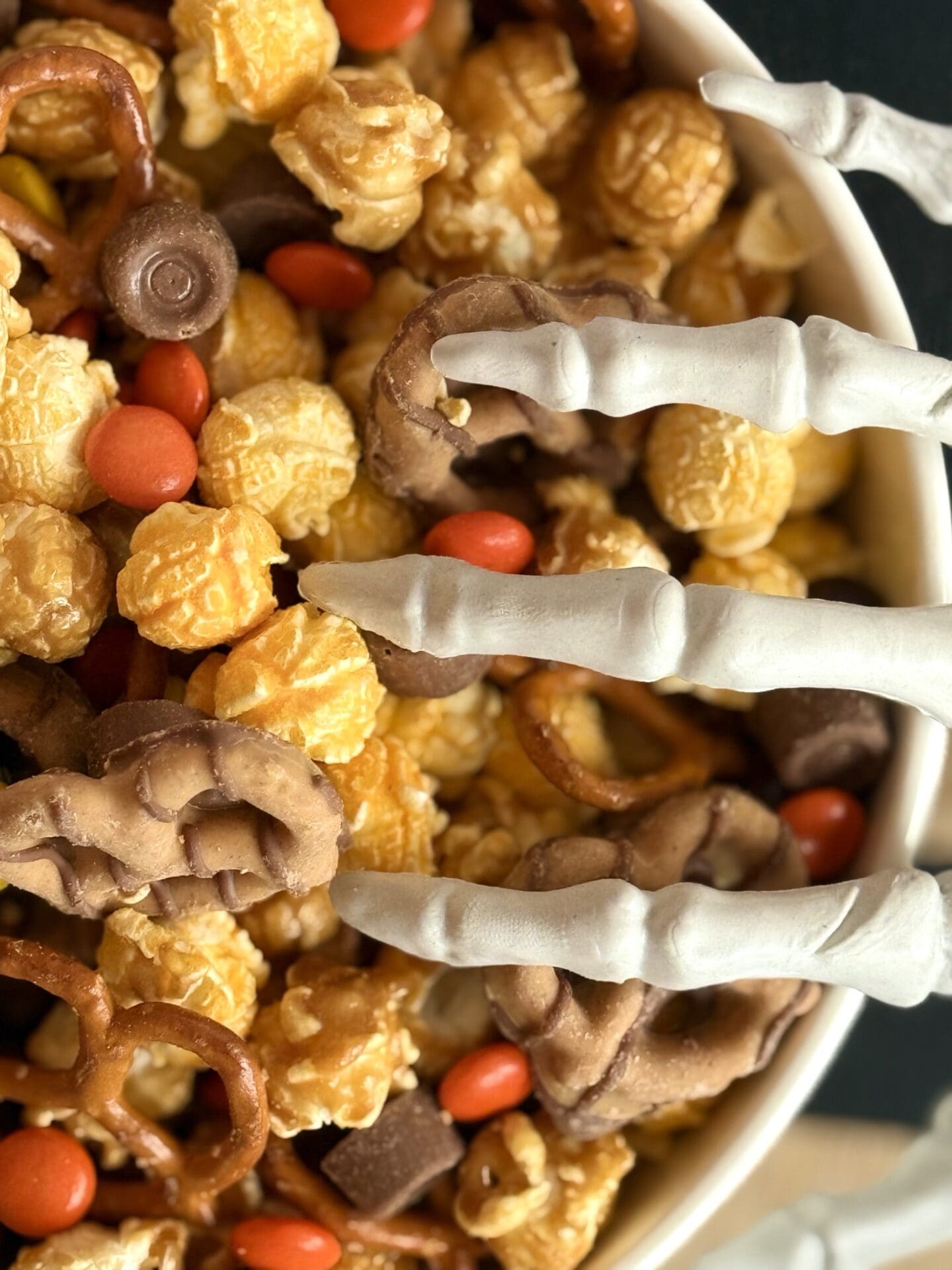 IMG_7137 A bowl of Monster Munch Halloween Snack Mix is seen close up with a skeleton hand creeping into the bowl from the side.