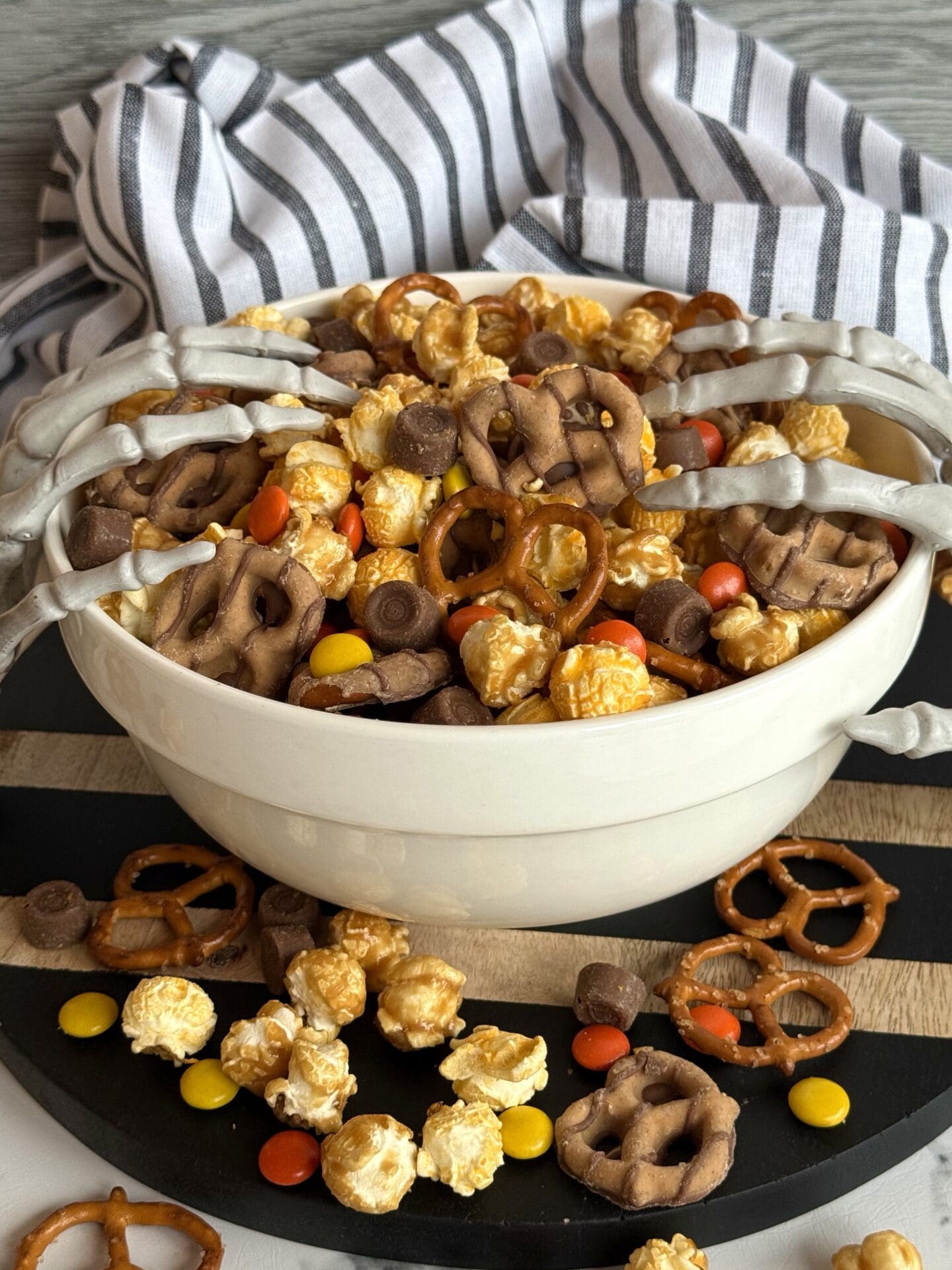 IMG_7140 A bowl of Monster Munch Halloween Snack mix spills over onto a black wooden board. Skeletons hands reach hands creep into the bowl from either side.
