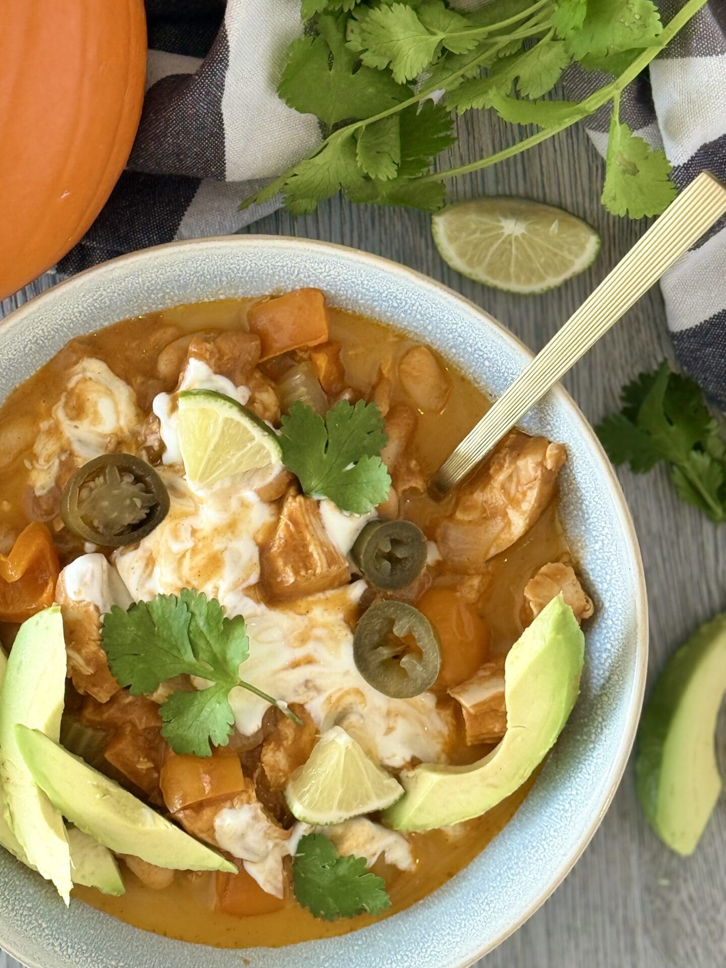 IMG_7210 A bowl of Pumpkin Chicken Chili is seen from above, generously garnished with avocado slices, jalapeño, lime, cilantro and sour cream.
