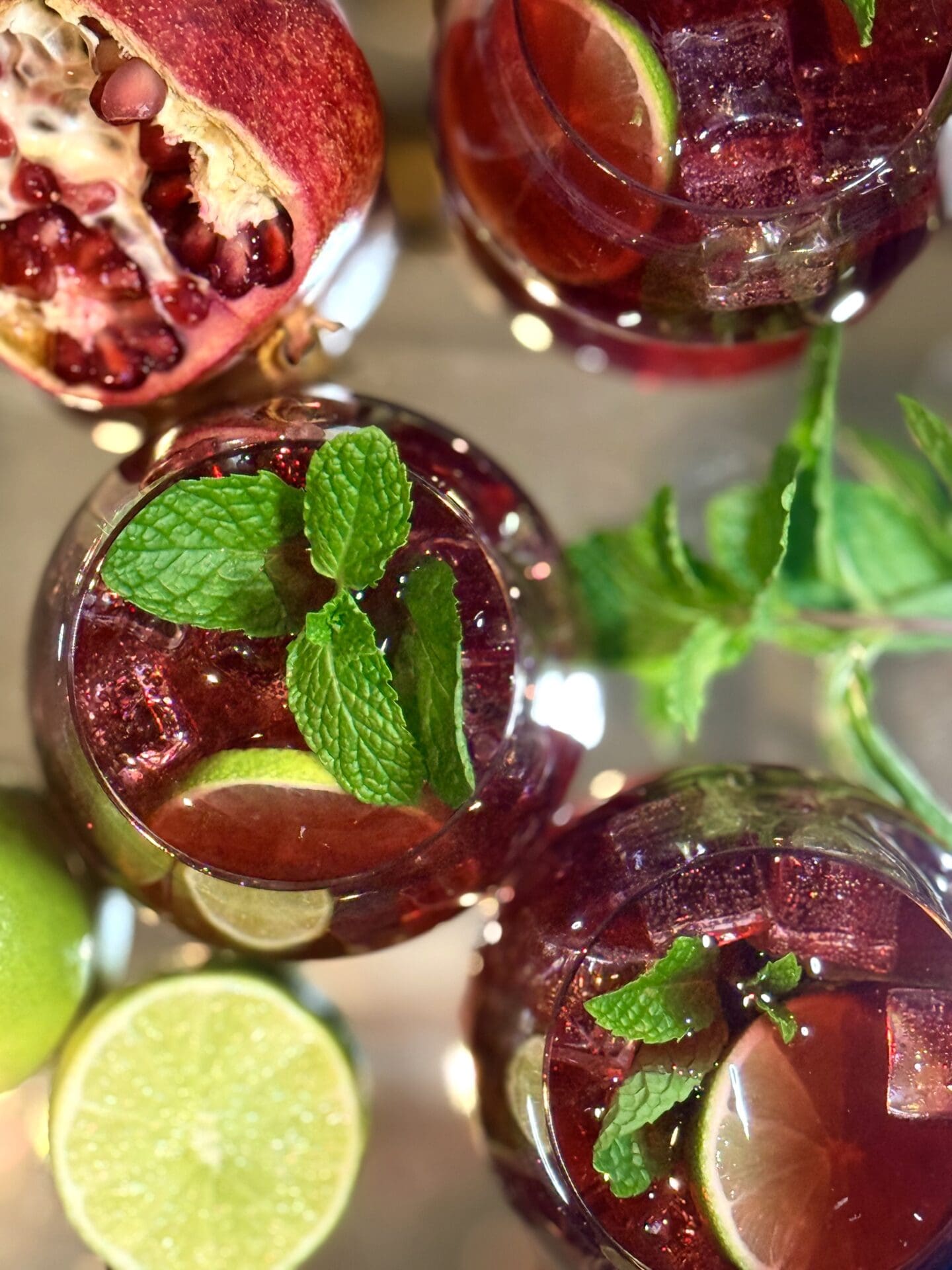 IMG_7797 Glasses of ruby red pomegranate lime mocktail are seen from above, garnished with fresh mint, lime and pomegranate.