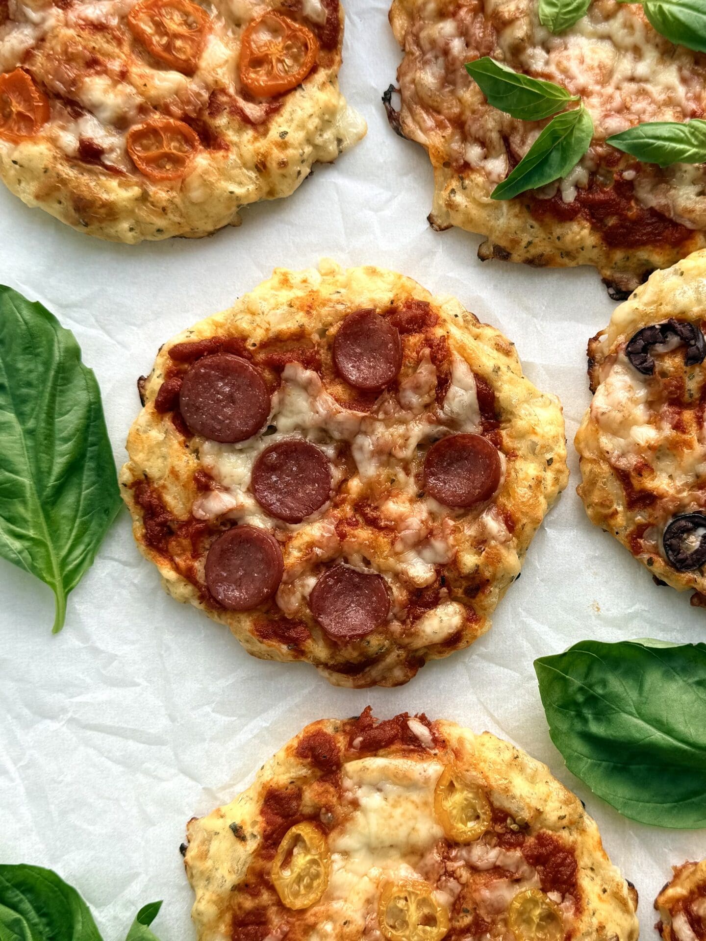 Baked cottage cheese pizza buns are seen from above on a baking sheet. The pizza in the centre is topped with pepperoni, whereas the surrounding pizza buns feature an assortment of colourful vegetables.