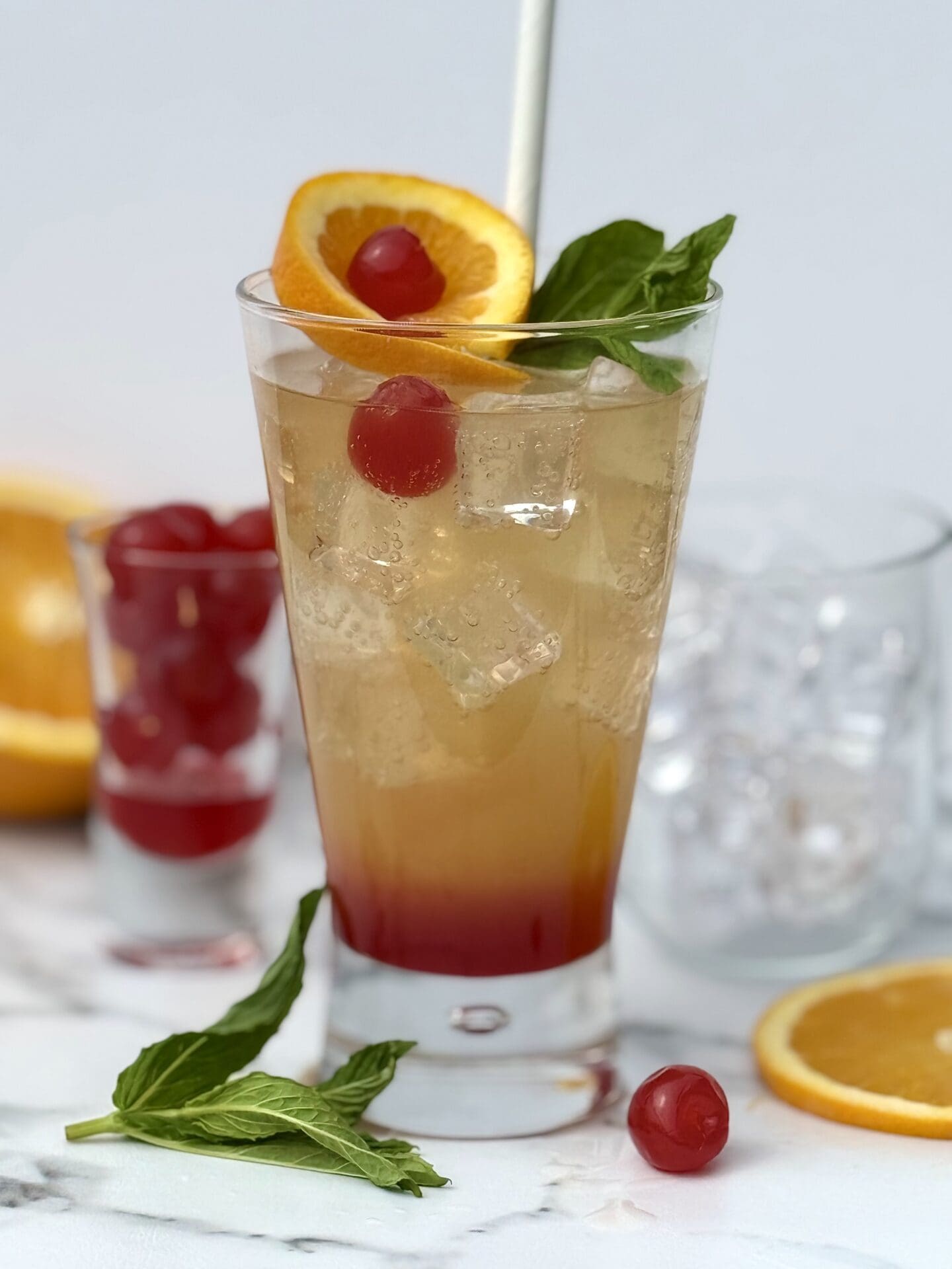 A Shirley Temple drink shows off its pretty layers of grenadine, orange juice and ginger ale, in a lavishly garnished glass.