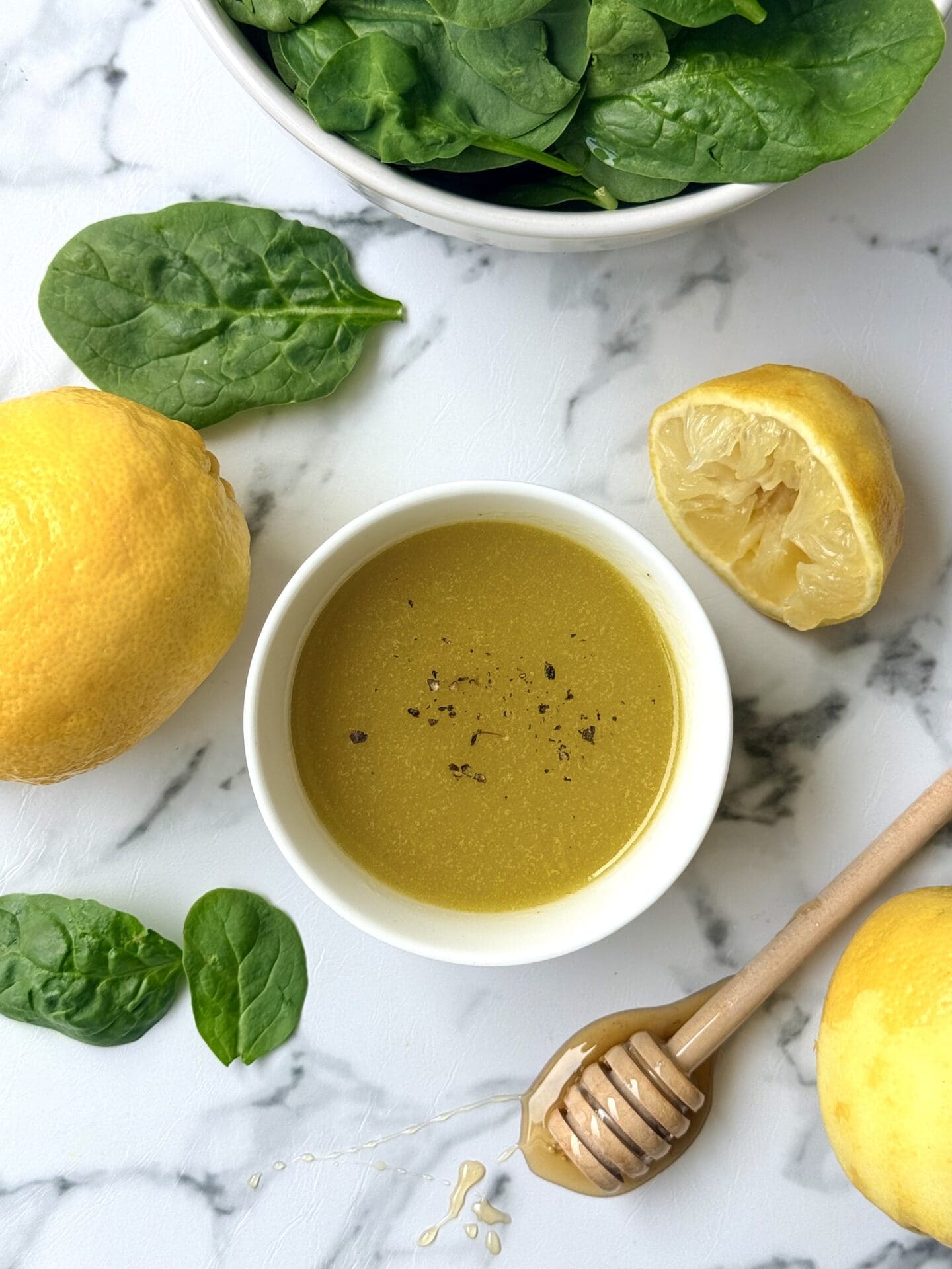 IMG_8645 A bowl of Mediterranean Lemon Vinaigrette is seen from above, surrounded by fresh lemons, honey and baby spinach.