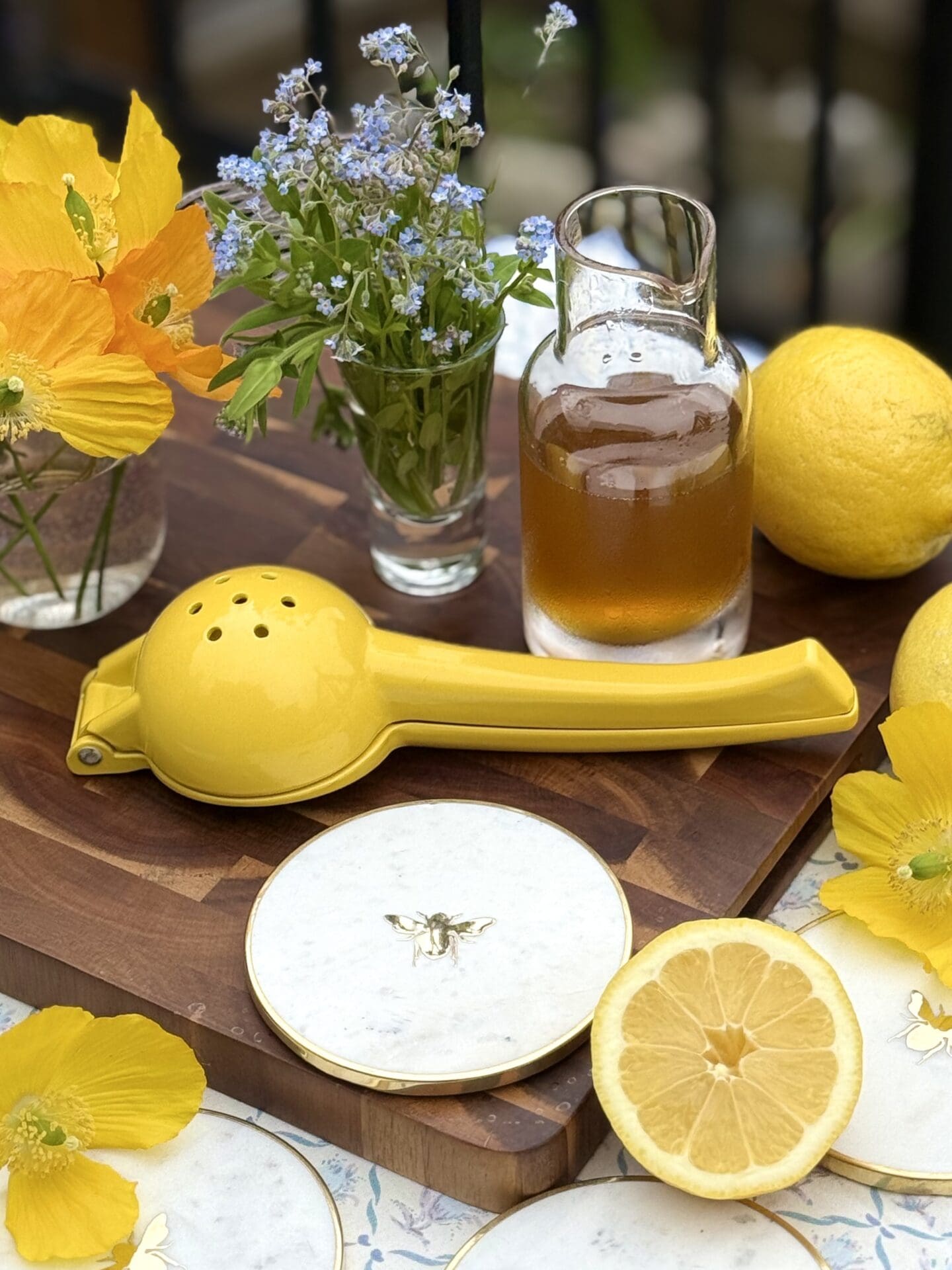 The ingredients for a Bee’s Knees cocktail sit on a wooden board, ready for use. Honey simple syrup, fresh lemons and spring flowers can be seen.