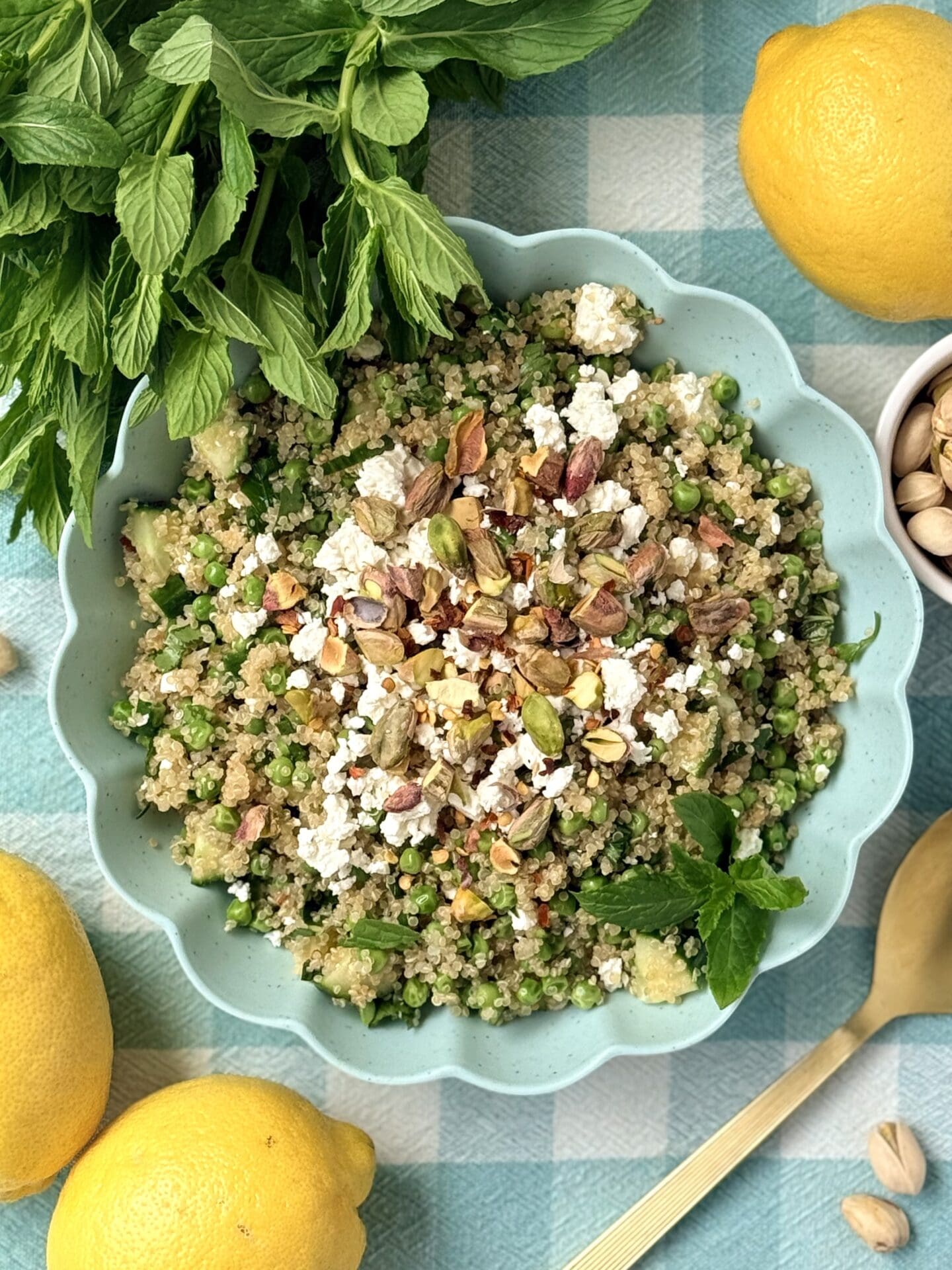 A lemon quinoa salad with fresh herbs, pistachios and feta cheese is seen from above surrounded by a display of its ingredients.