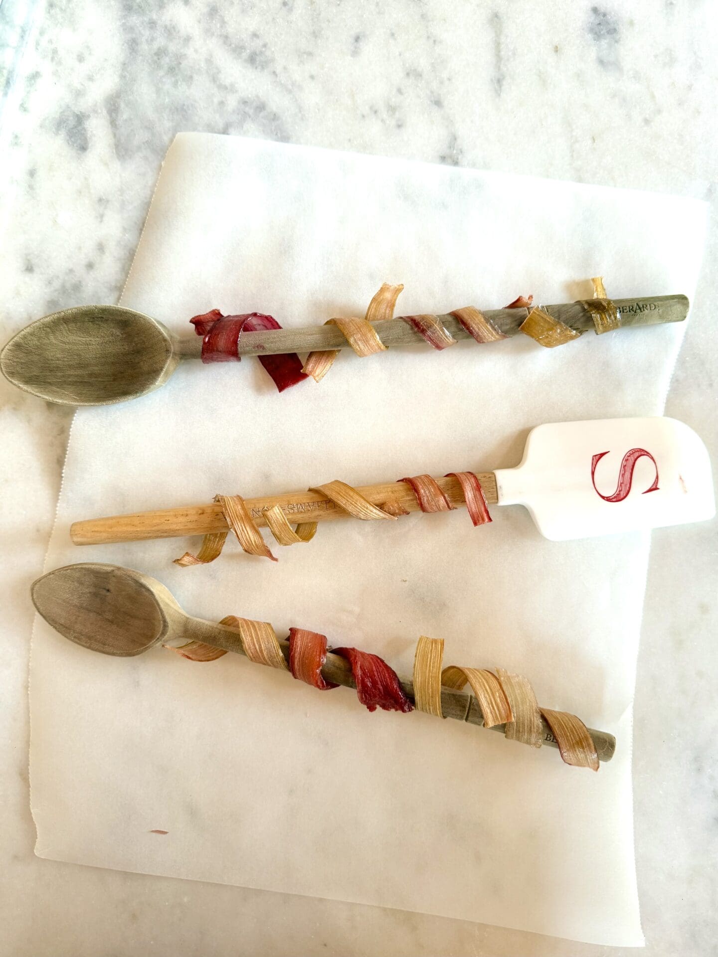 Strips of candied rhubarb are wrapped around the handles of wooden spoons to shape them into spirals.