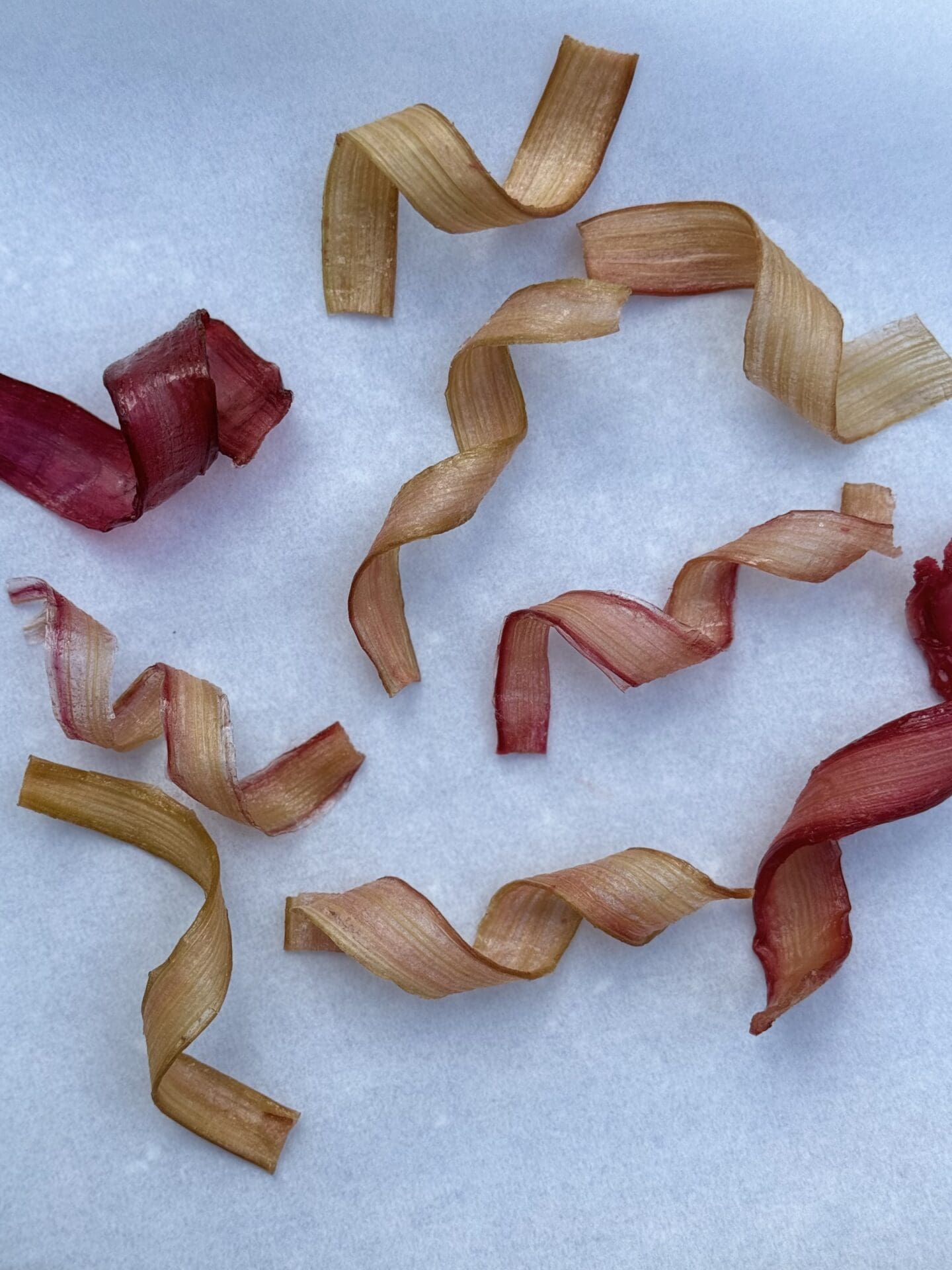 Candied Rhubarb Ribbons in different shades of pink and red are twisted into spirals and are seen from above on a white background.