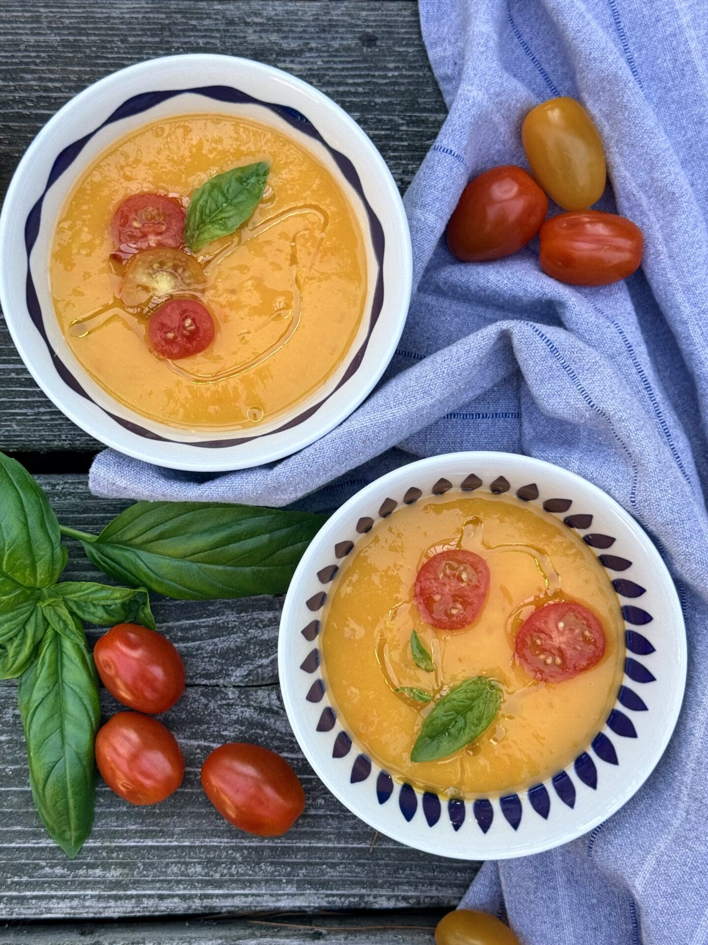 IMG_9799 Bowls of Yellow Tomato Gazpacho are surrounded by a blue linen napkin, fresh basil and tomatoes.