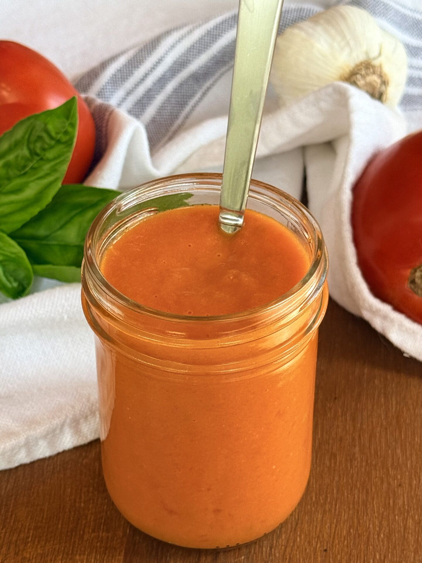 A jar of fresh tomato sauce A jar of bright orange fresh tomato sauce is seen on a table, surrounded by fresh tomatoes, garlic and basil.