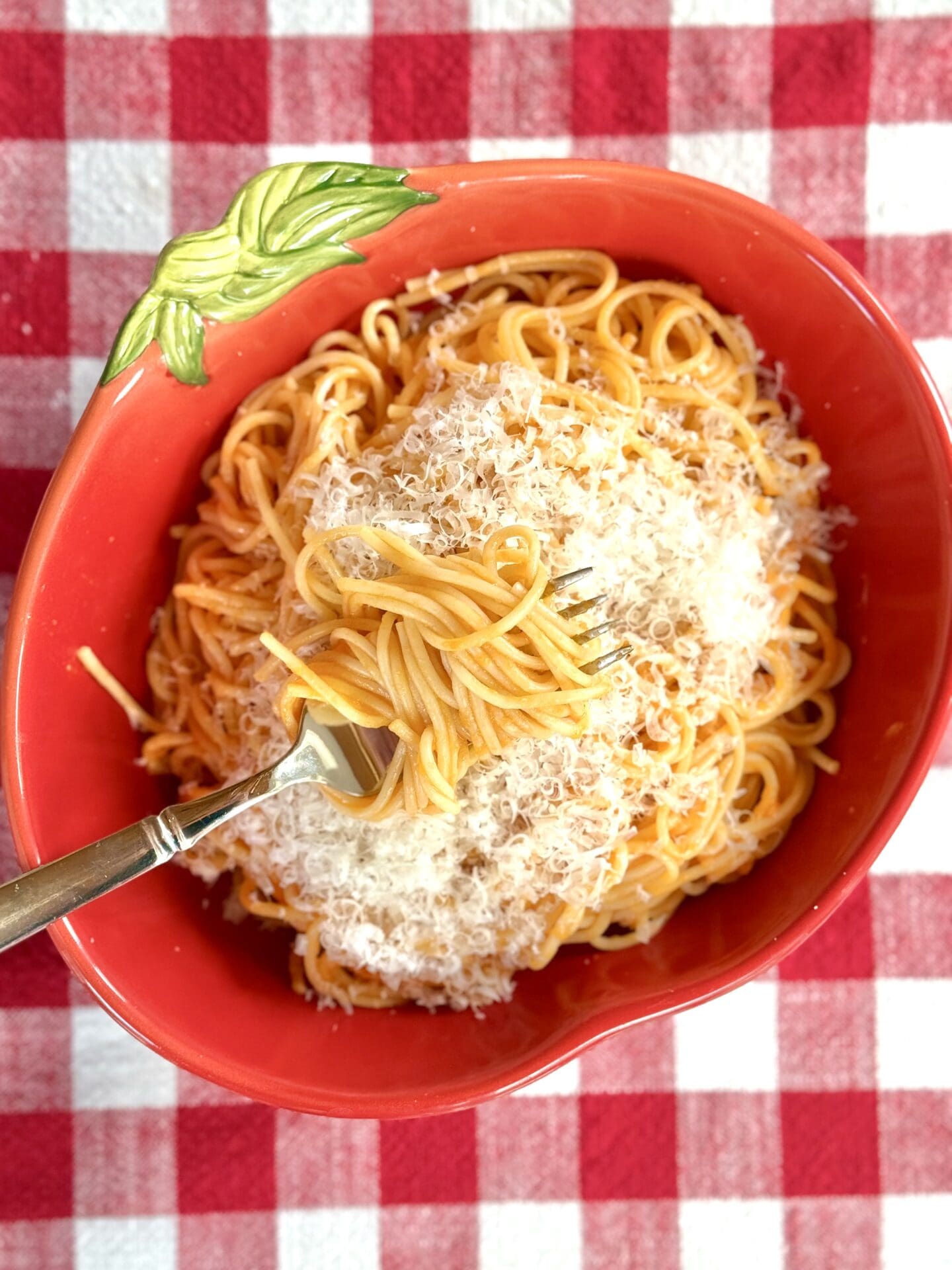 Spaghetti al Pomodoro in a tomato bowl A tomato shaped bowl filled with spaghetti with fresh tomato sauce and lots of fresh tomato sauce is seen from above on a red checkered table cloth.