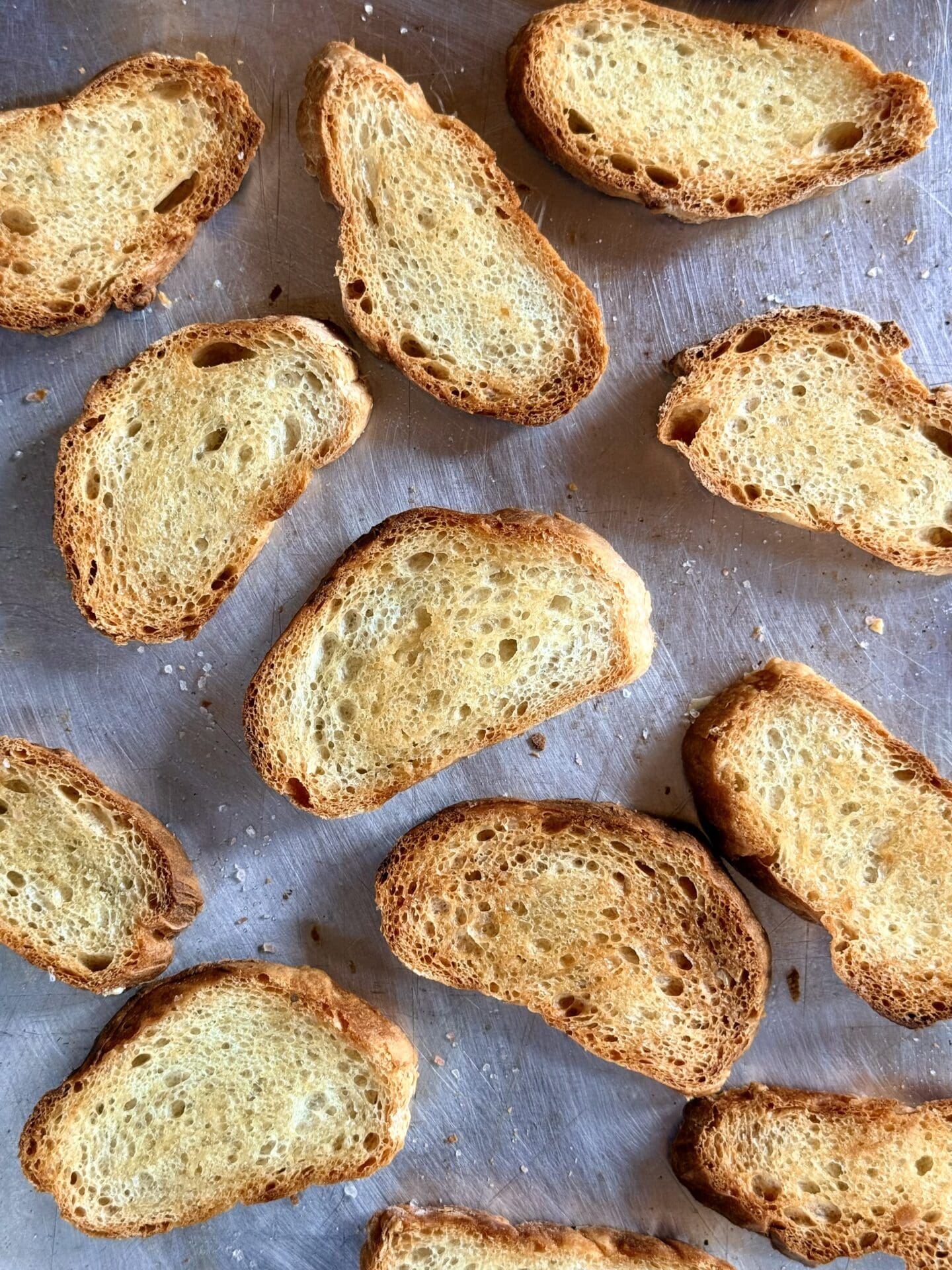 Crostini are seen from above on a baking sheet, fresh from the oven.