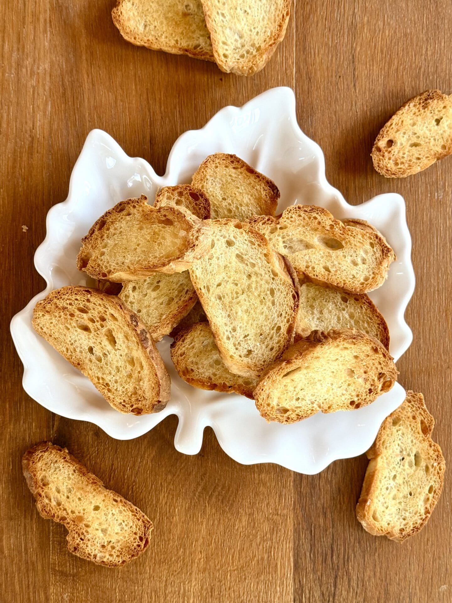 A maple lead shaped plate holds crostini that spill out onto the wood table below.