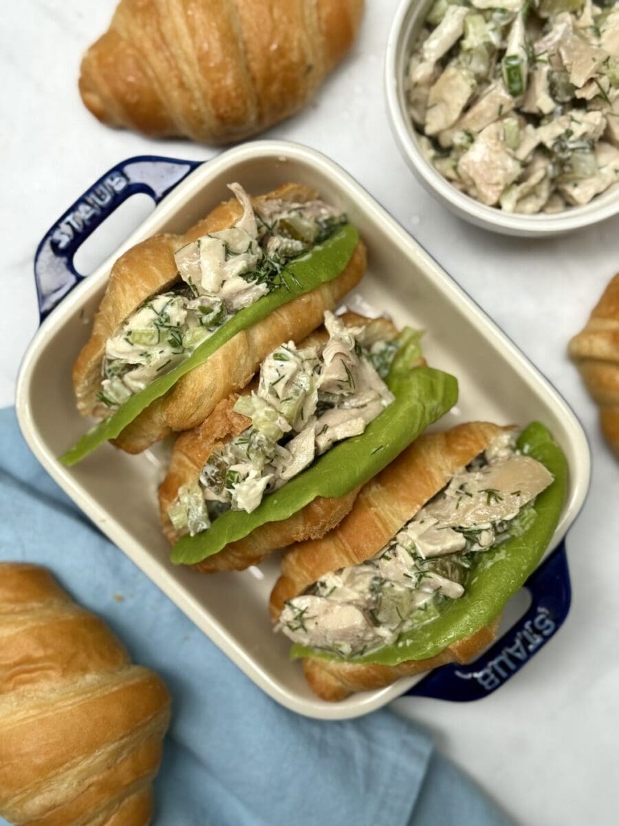 Three flaky croissants are seen from above, stuffed with dill pickle chicken salad and fresh lettuce.