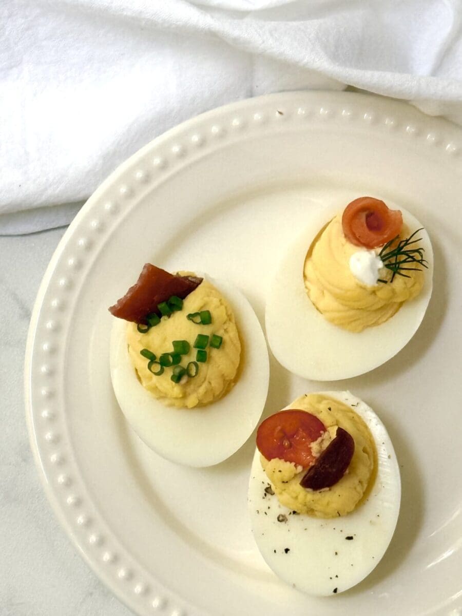 Three deviled eggs, with different toppings sit on a cocktail plate ready to be eaten.