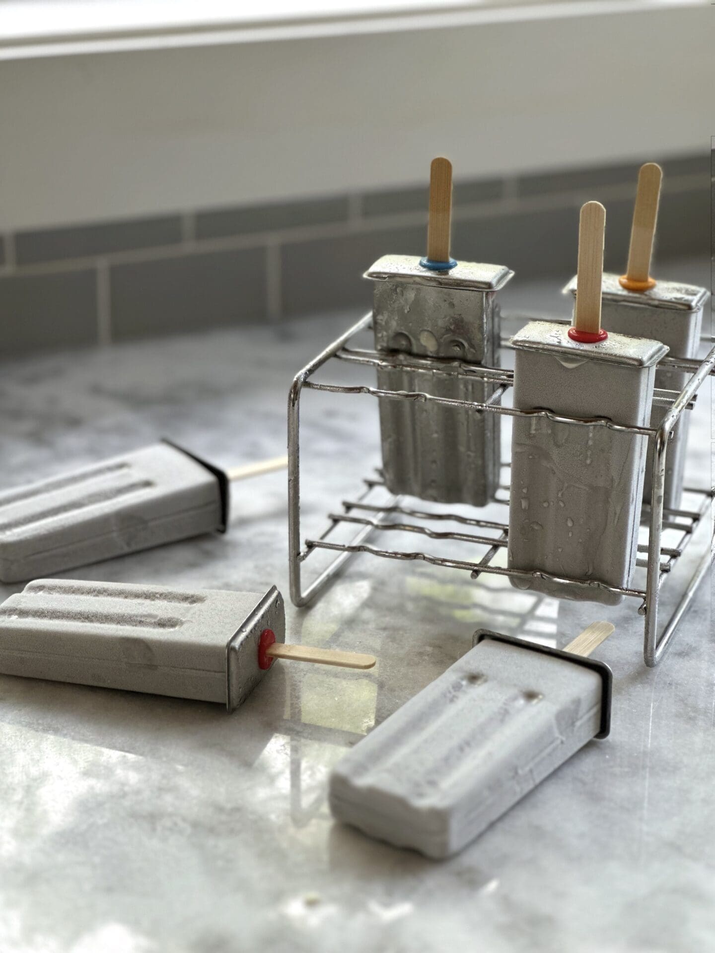 IMG_8662 Homemade popsicles in frosty stainless steel popsicle moulds sitting on a white marble counter with grey tile backsplash in the background