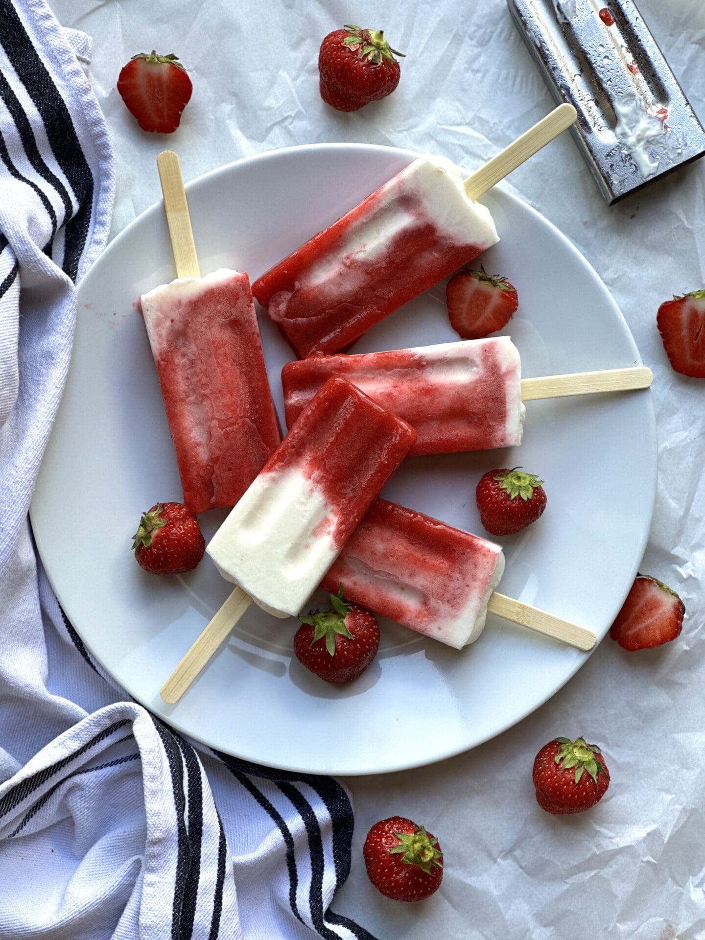 Plate of strawberries and cream breakfast popsicles surrounded by fresh strawberries.