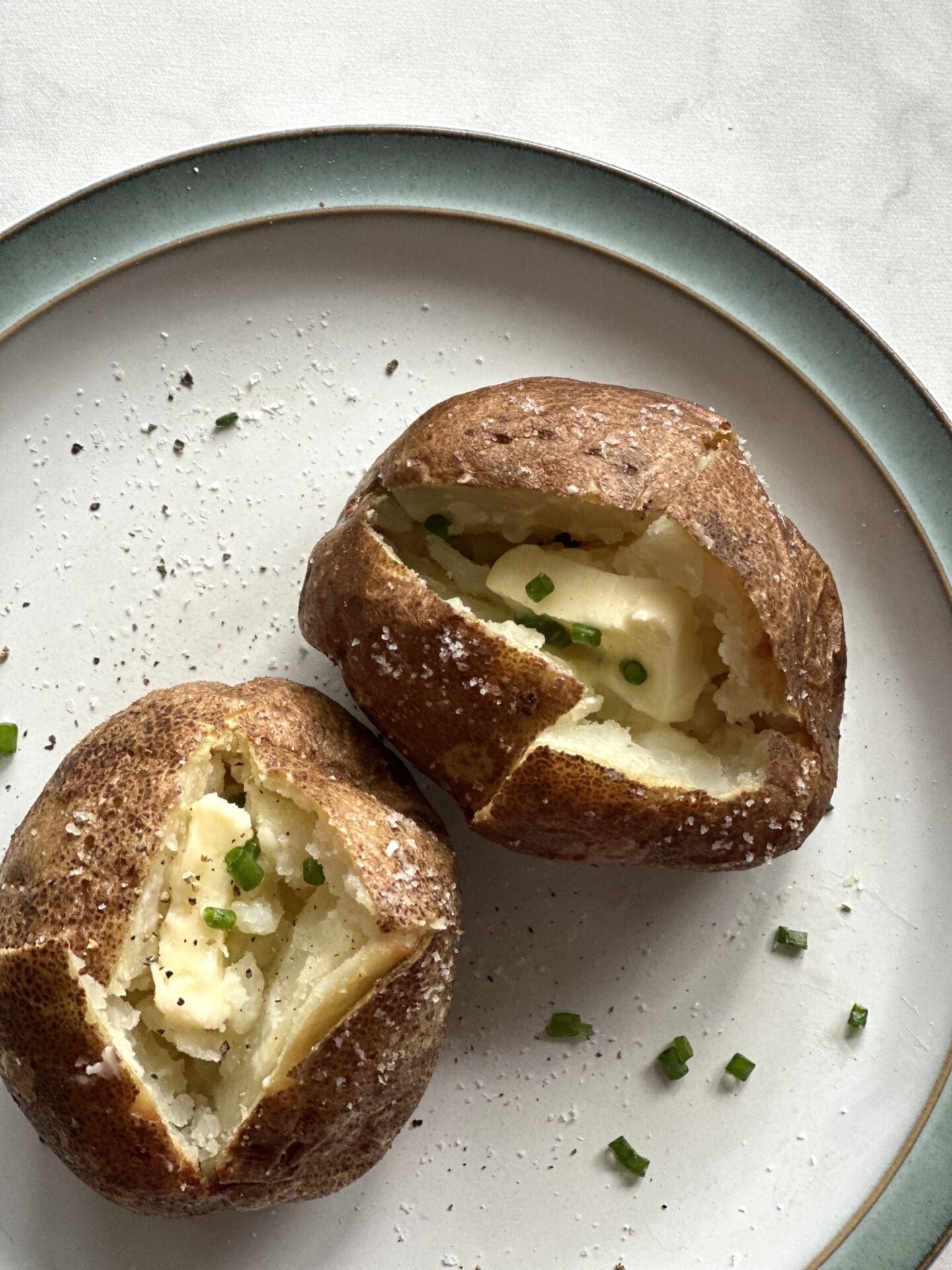 Baked potatoes seen from above Perfect, crispy skinned baked potatoes and seen from above, split open and filled with a generous pat of butter and garnished with chopped chives.