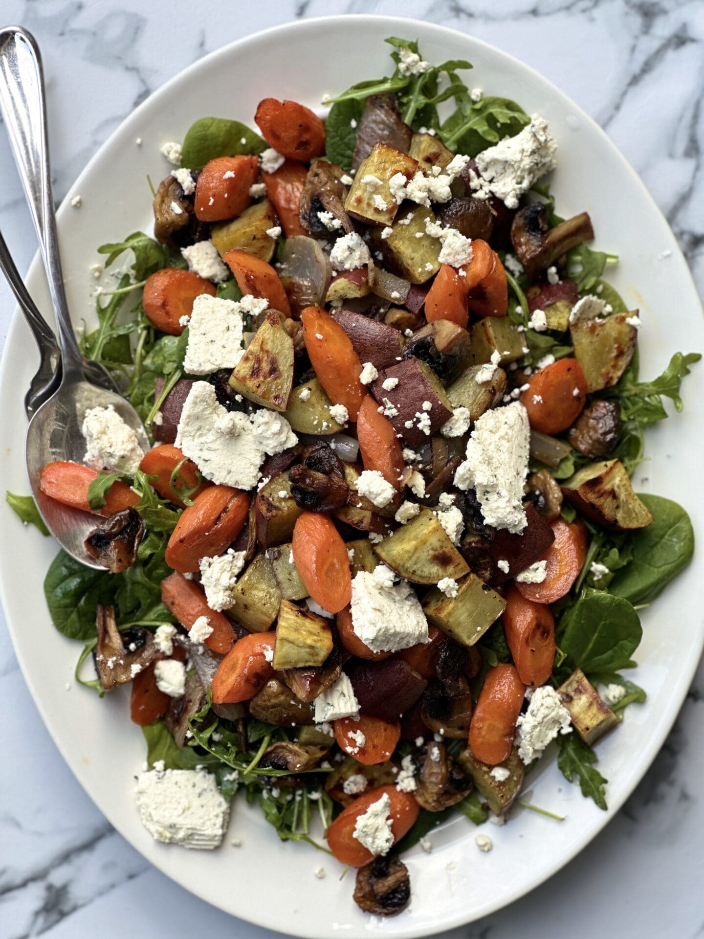 A large platter of Warm Roasted Vegetable and Boursin Salad is seen from above on a white marble table.