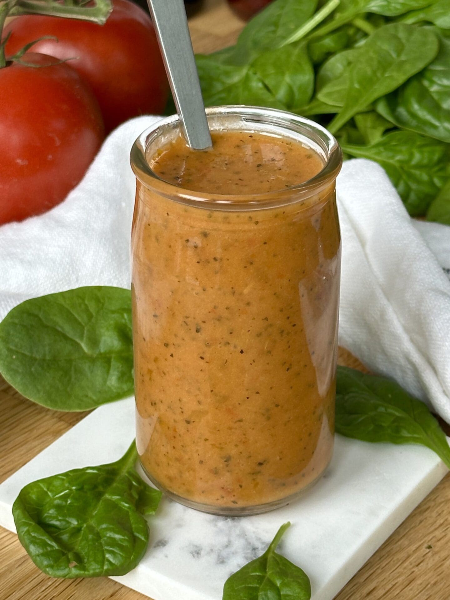 IMG_3652 A jar of Sundried Tomato Vinaigrette sits on a wood table surrounded by bright red tomatoes and salad greens
