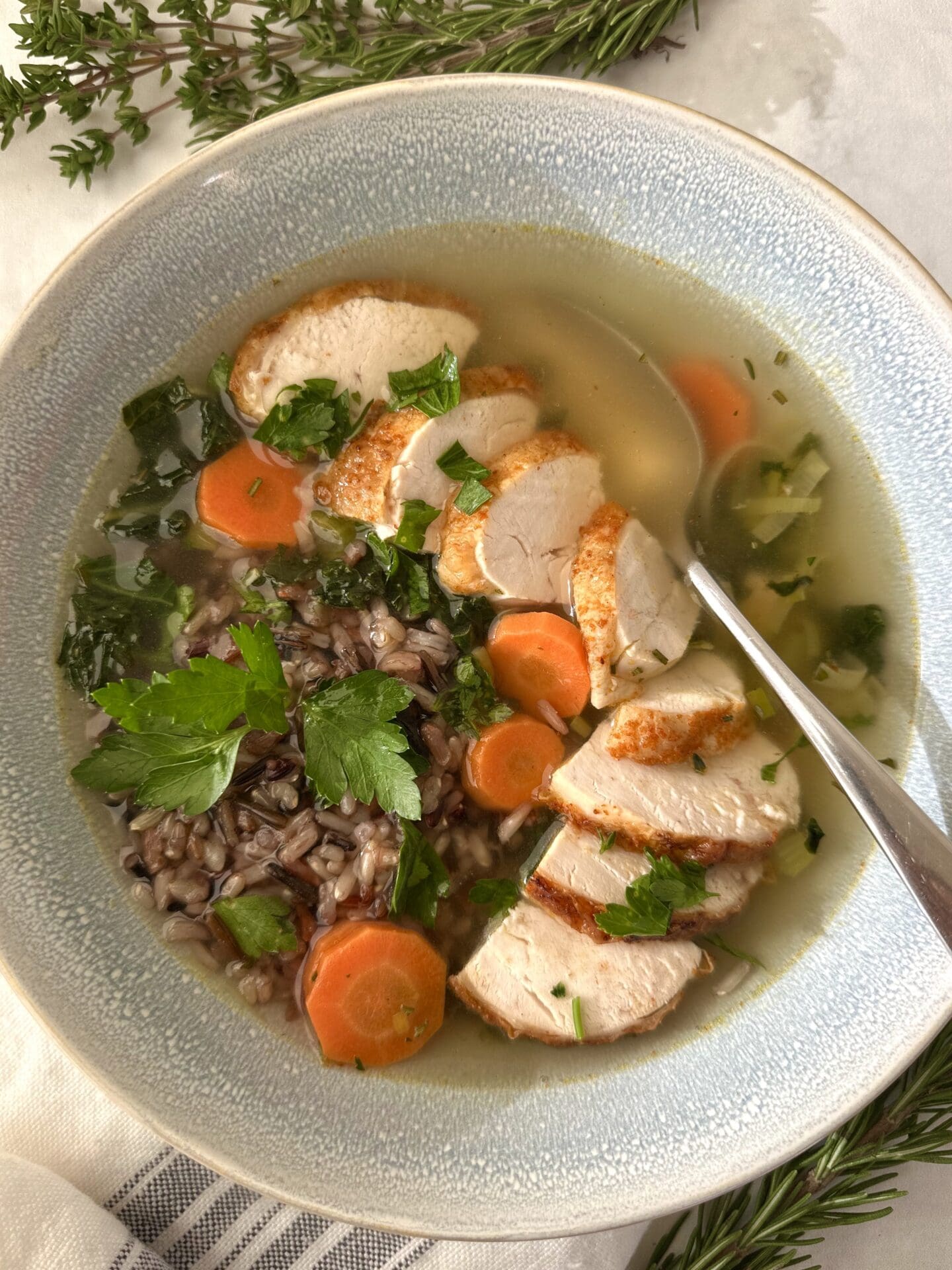 A bowl of Turkey, Leek and Wild Rice Soup is seen from above, garnished with large slices of juicy turkey and fresh parsley