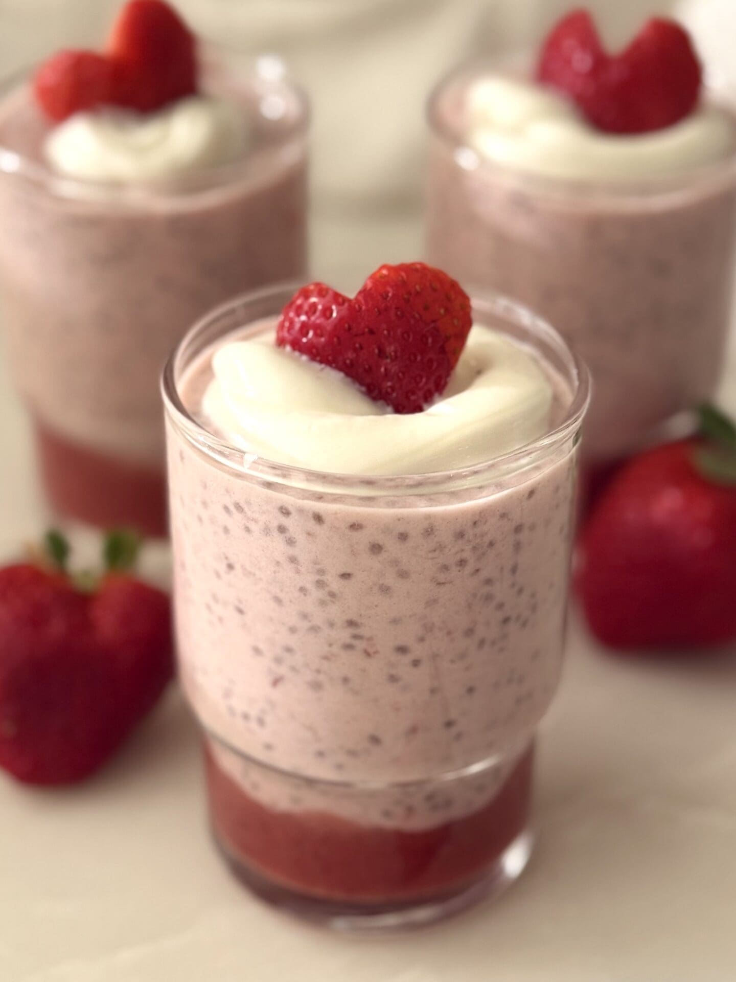 A glass jar holds a Strawberry Chia Seed Pudding with a layer of strawberry puree. The pudding is garnished with a dollop of white yogurt and a heart shaped strawberry slice.