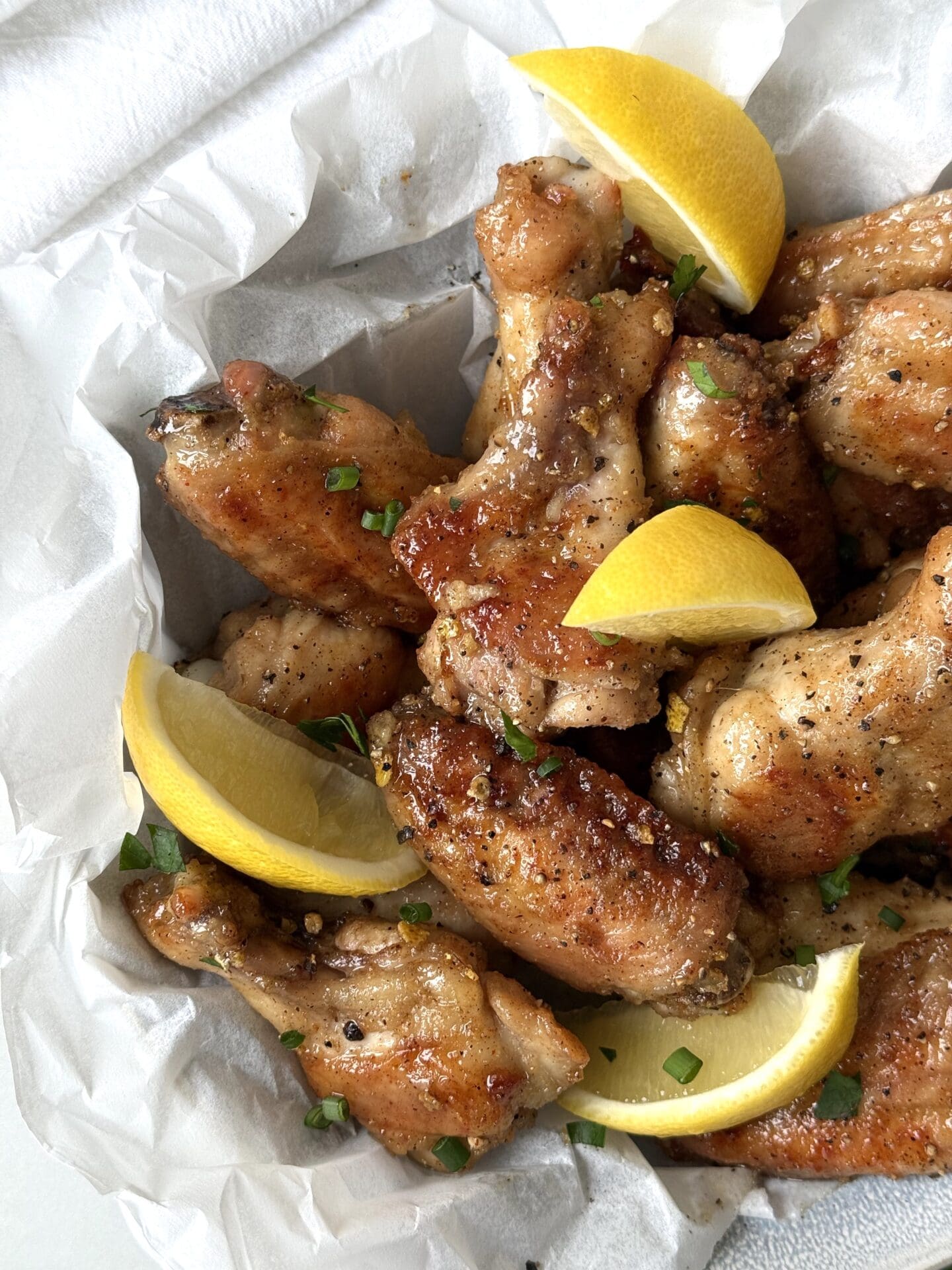 A parchment paper lined bowl of Sweet and Tangy Lemon Pepper Chicken Wings is seen from above, garnished with fresh lemon wedges