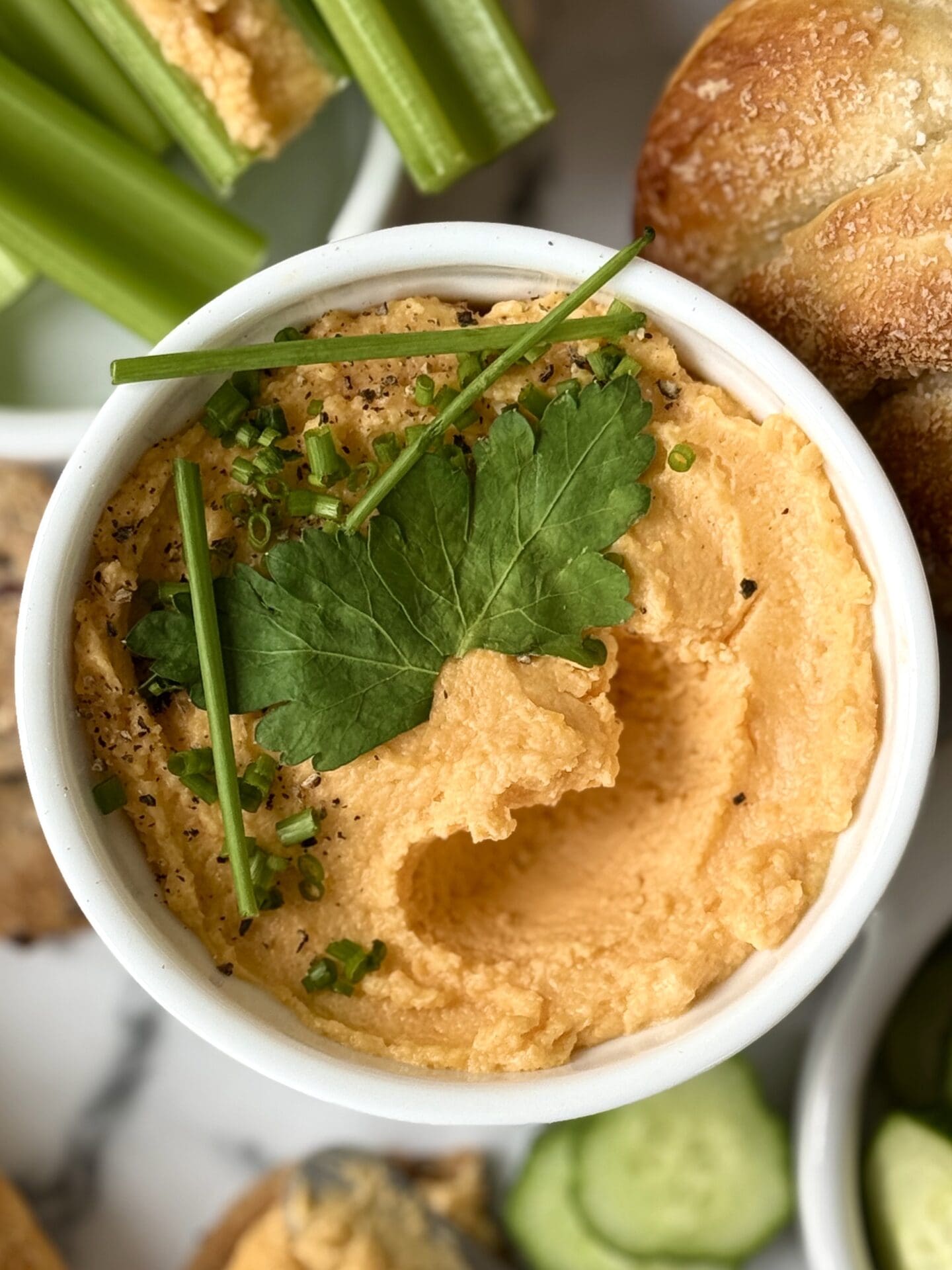 A dish of orange Pub Style Beer Cheese is seen from above, in close up, garnished with fresh green herbs.