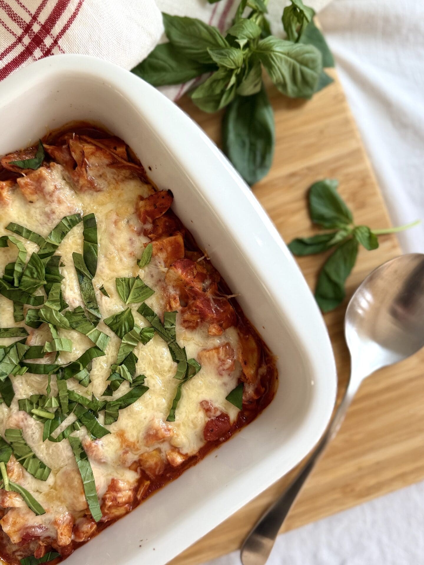 A Healthier Chicken Parmesan Casserole is seen fresh from the oven, with a bubbling cheese top and fresh basil garnish.