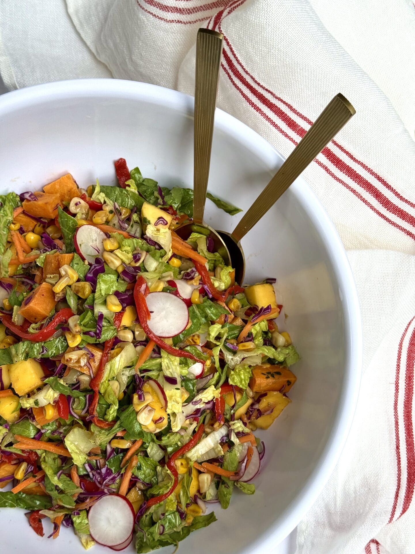 A bowl of colourful Mexican Chopped Salad is seen from above in a white bowl, surrounded by a red and white striped cloth.