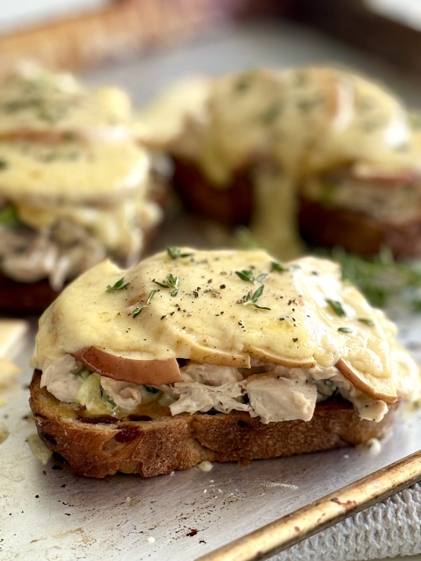 Chicken and Apple Melts with Smoked Cheddar are seen hot from the oven with melting cheese dripping down over the edges of the sandwiches.