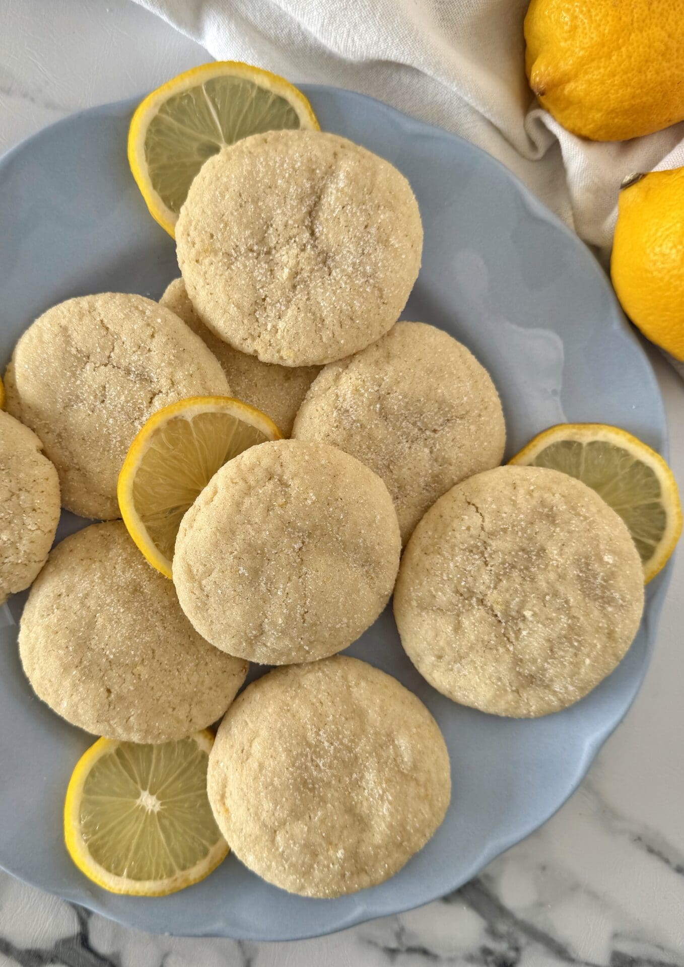 IMG_7402 A light blue plate is filled with soft and chewy lemon sugar cookies. Slices of fresh lemon are tucked around the cookies.