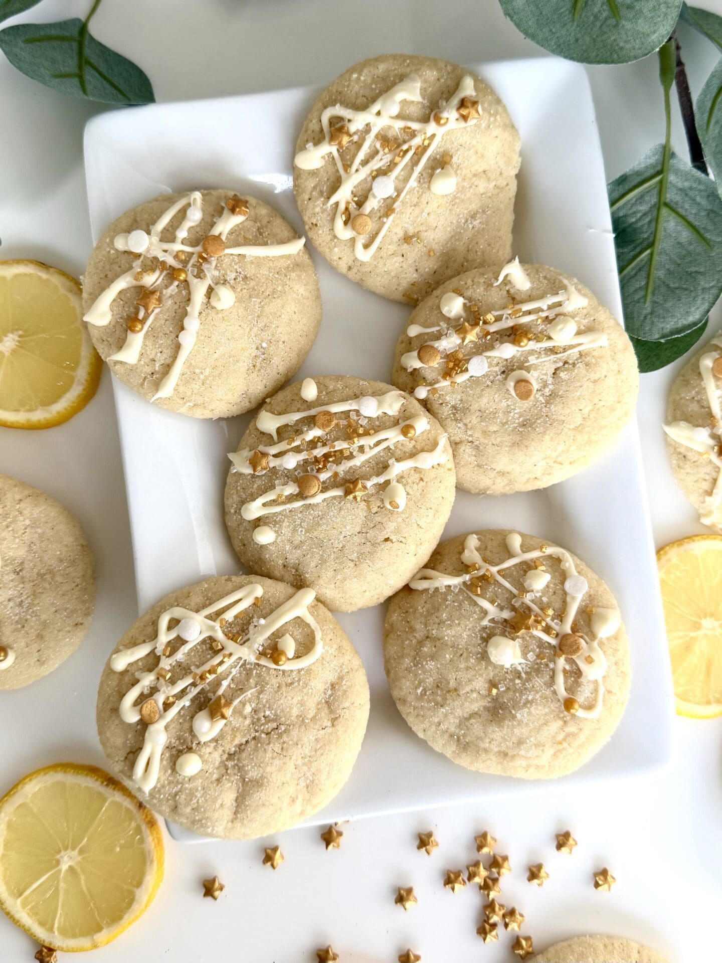 A platter of chewy and soft lemon sugar cookies is seen from above, dressed for the holidays with a drizzle of white chocolate and a dusting of gold sprinkles.