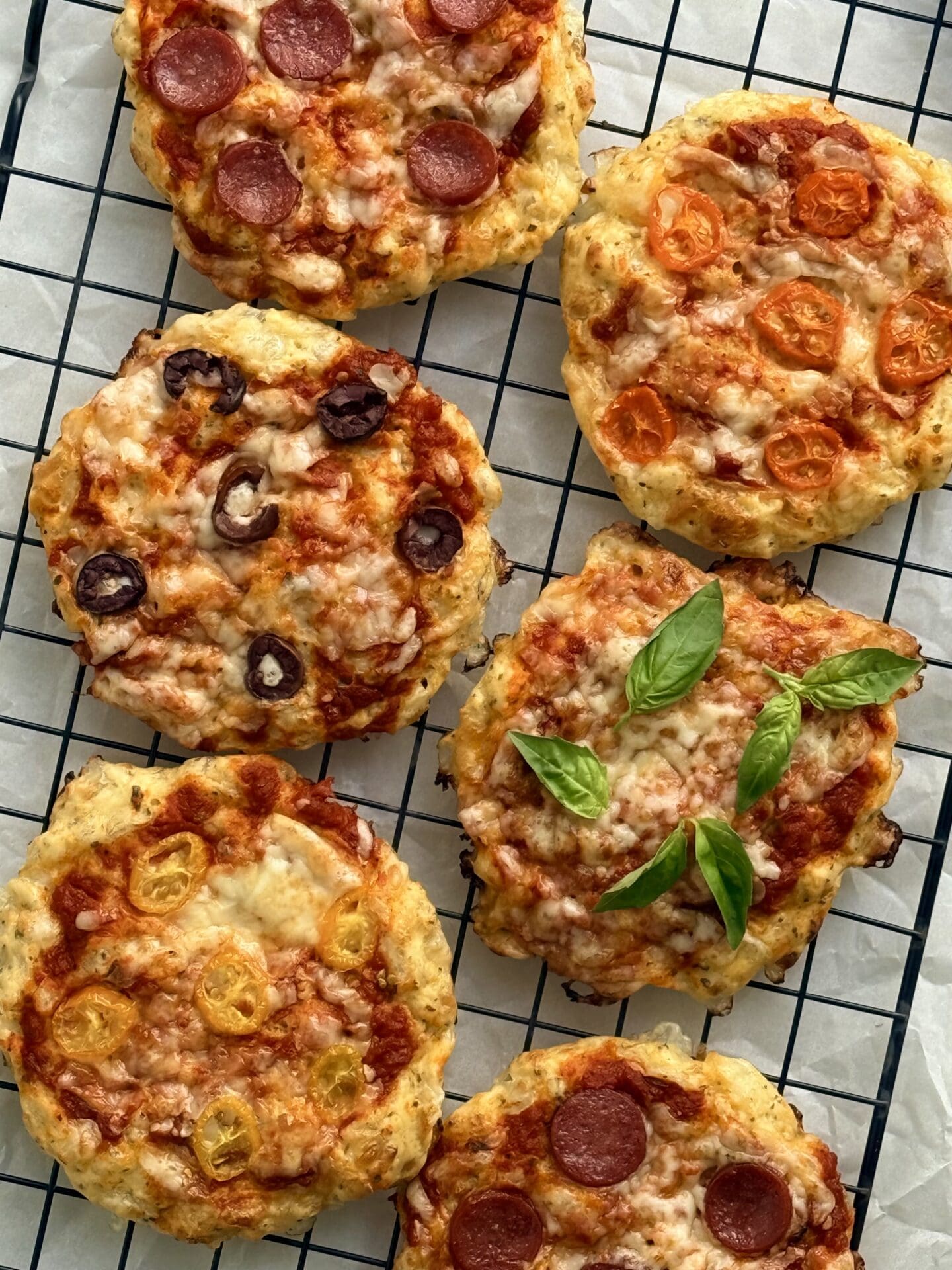 Cottage Cheese Pizza Buns featuring an assortment of toppings are seen from above, fresh from the oven, cooling on a black wire rack.