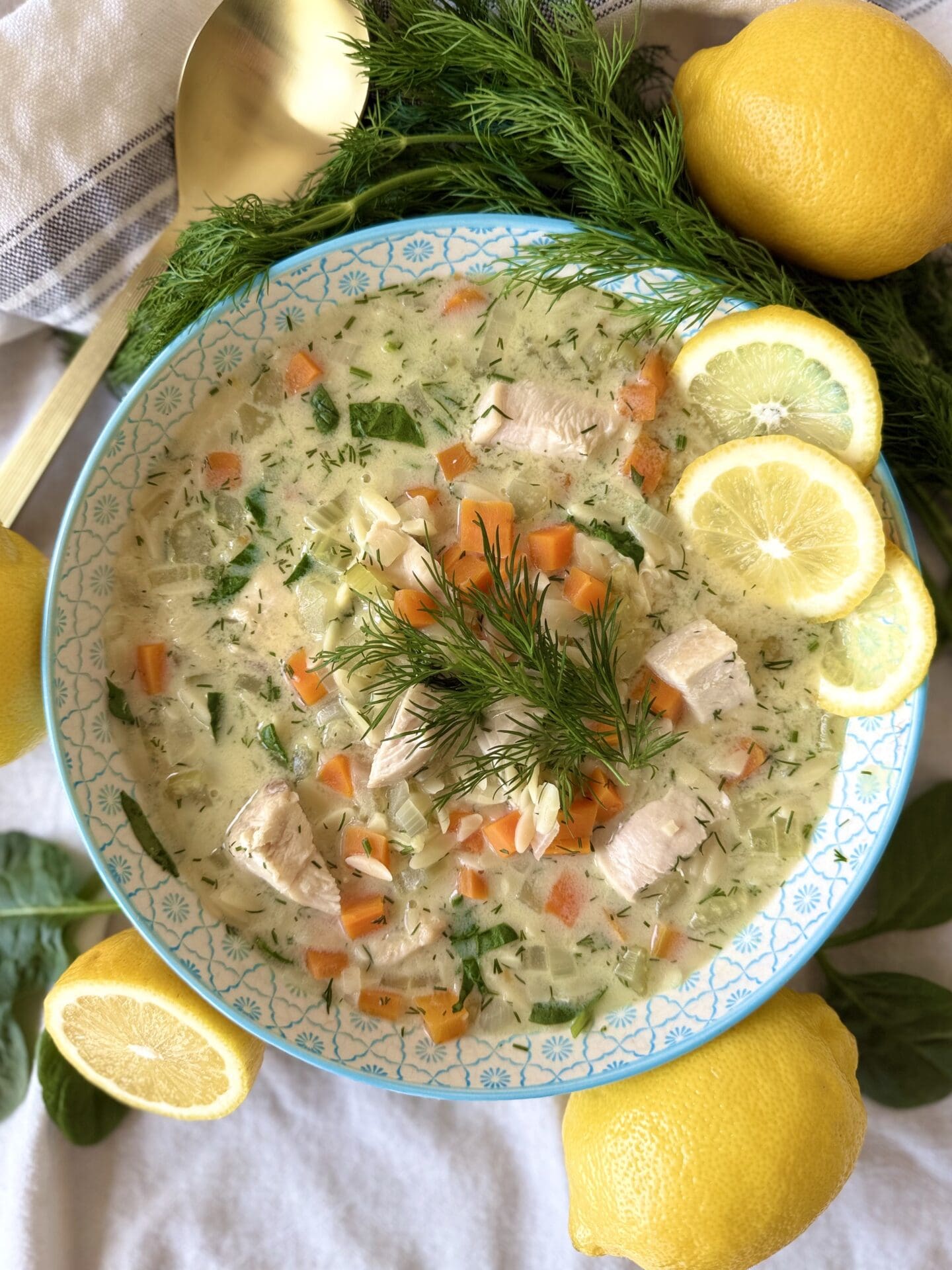 A bowl of Avgolemono soup is seen from above, brimming with fresh vegetables, juicy chicken and fresh lemon slices.