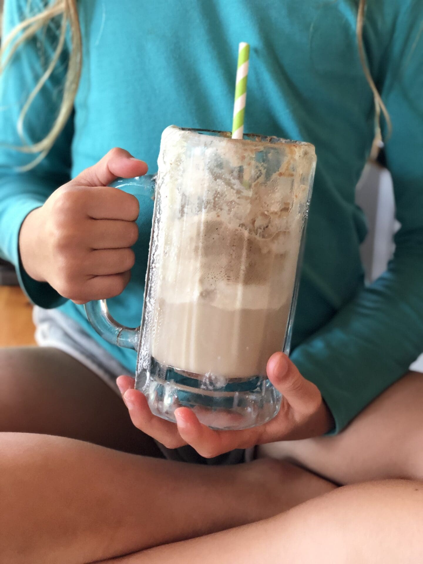 A child sits cross leg, holding a large frosty glass containing the remains of a root beer float