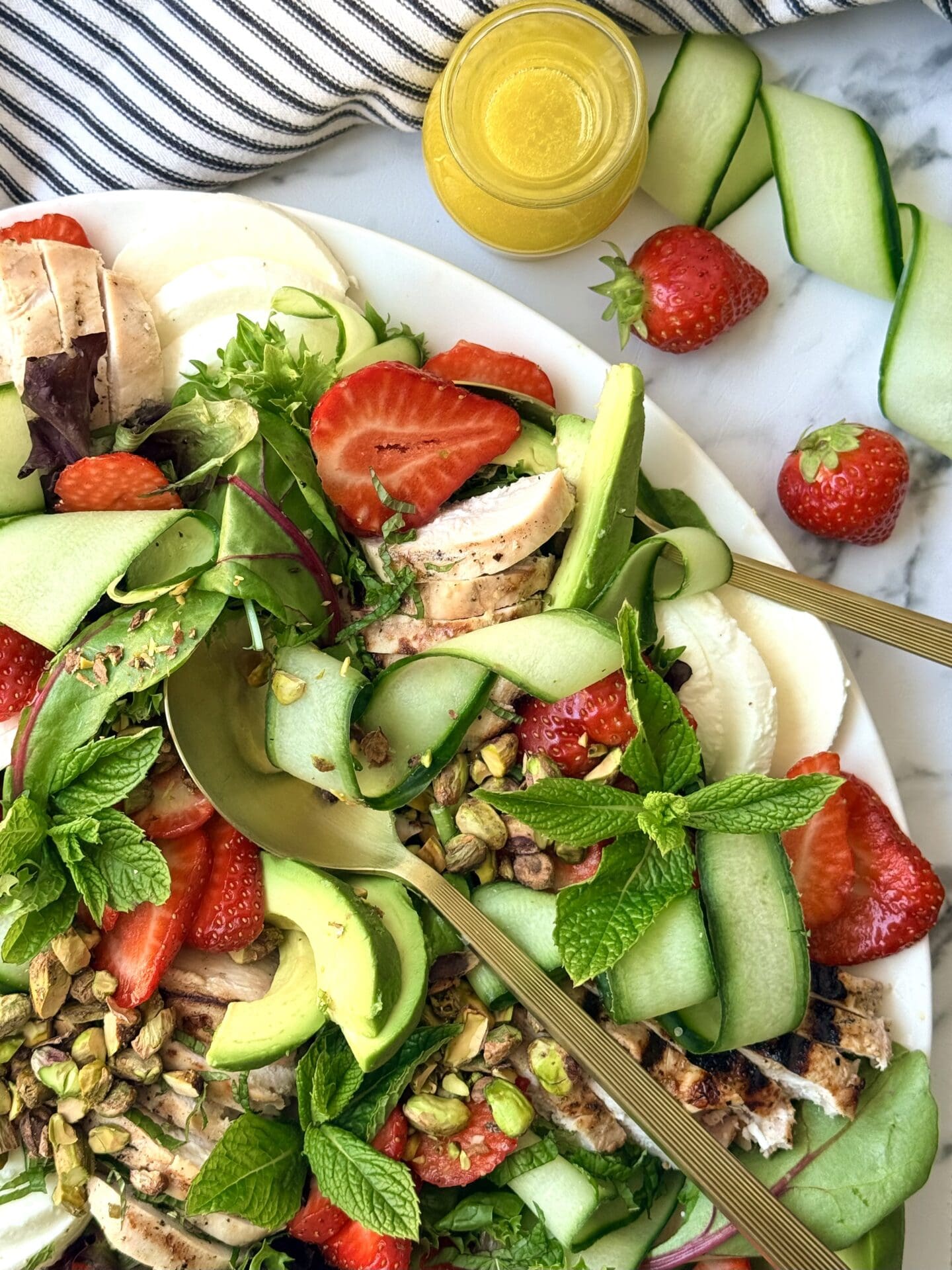 IMG_8887 A platter of Strawberry Cucumber Salad with Grilled Lemon Chicken is seen up close, showing off its vibrant mix of fresh summer vegetables, berries and fresh herbs.