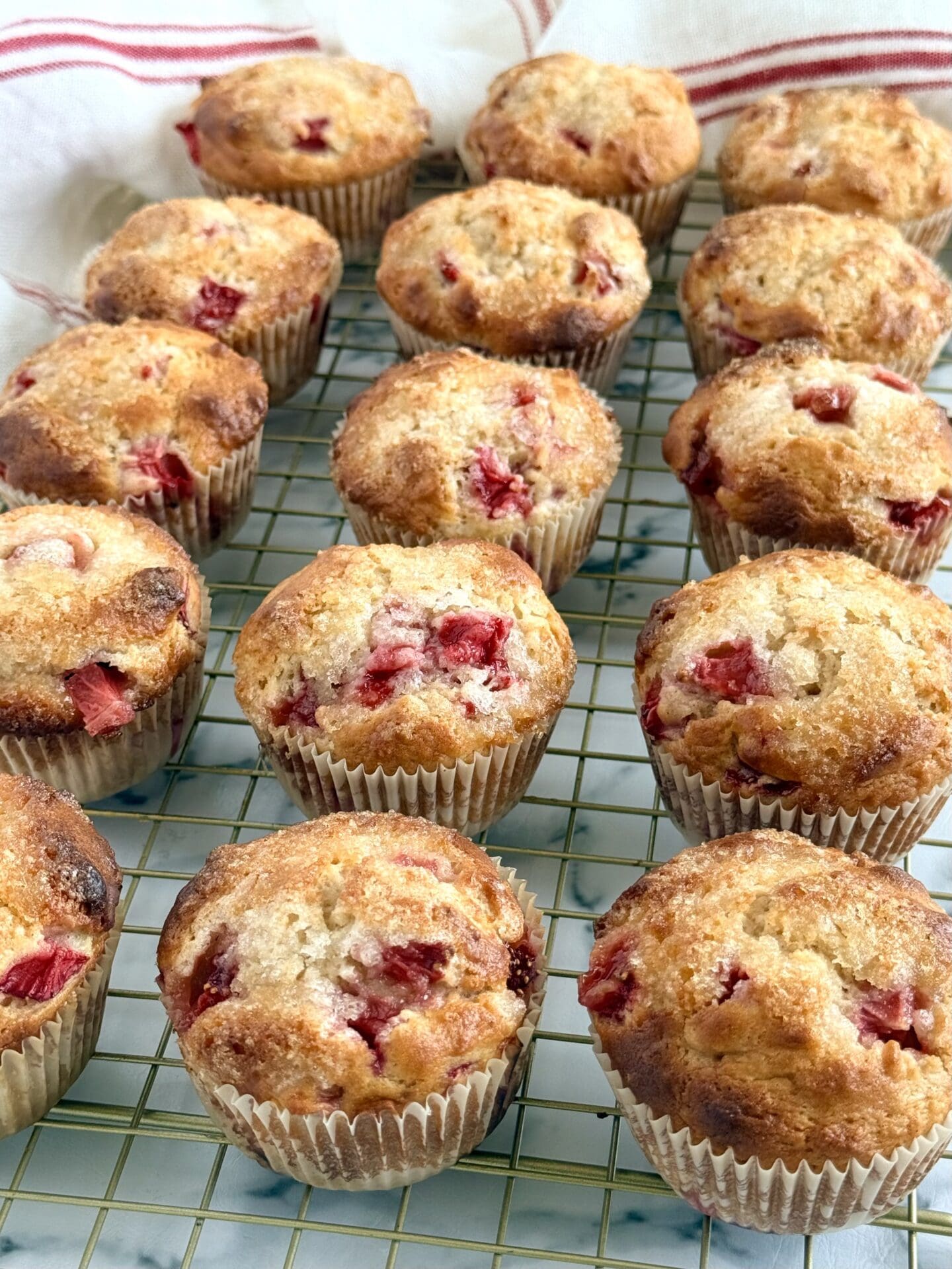IMG_8902 A batch of freshly baked strawberry yogurt muffins cools on a rack. The muffins show off their crispy-sweet tops studded with fresh strawberries.