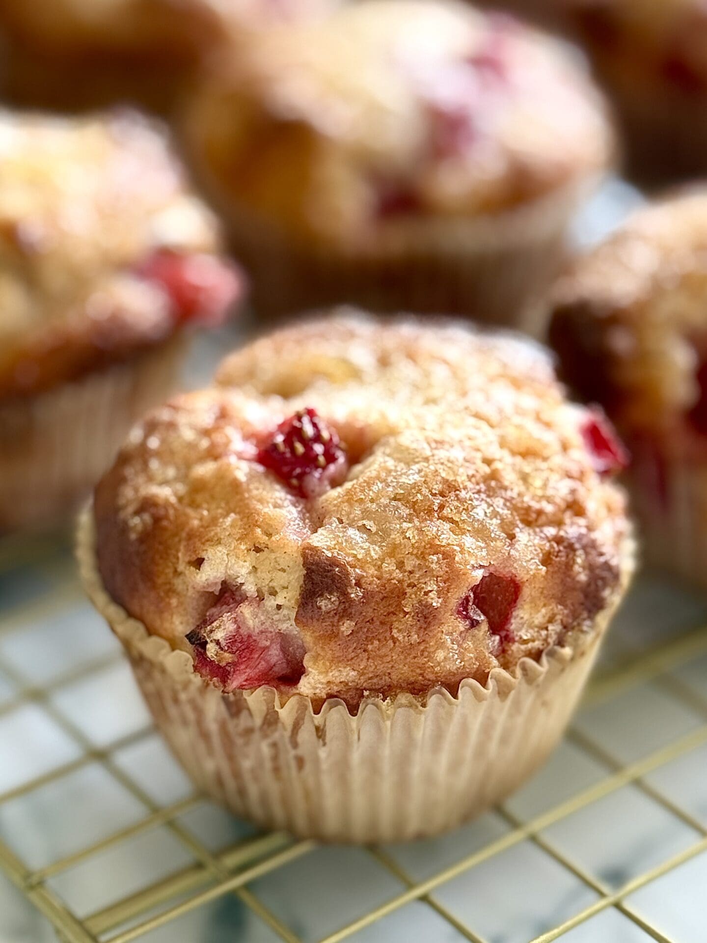 IMG_8908 A freshly baked strawberry yogurt muffin is seen close up, showing its crispy lemon sugar coated top, and pieces of juicy strawberry.